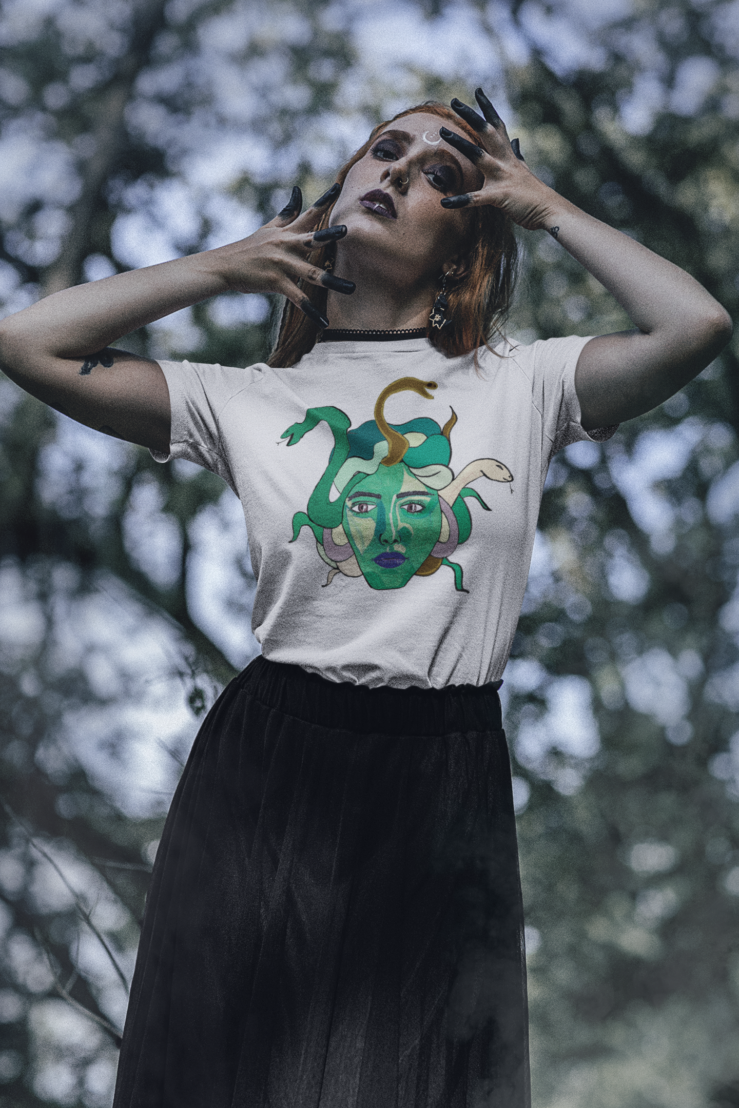Tattooed woman posing in a forest with hands near her face, wearing a white Medusa t-shirt by GrungePup Gallery