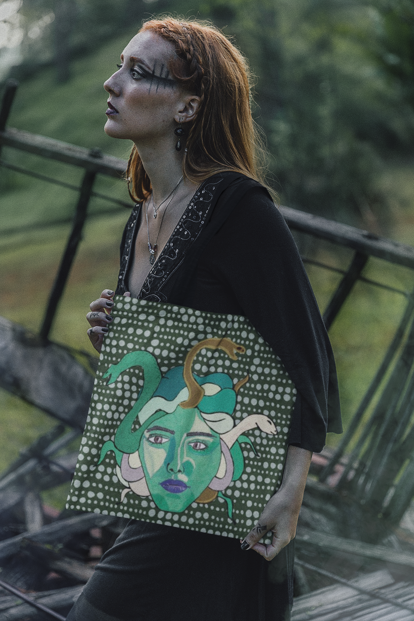 Woman with graphic makeup holding a Medusa all-over print tote bag with a dark green dotted background by GrungePup Gallery