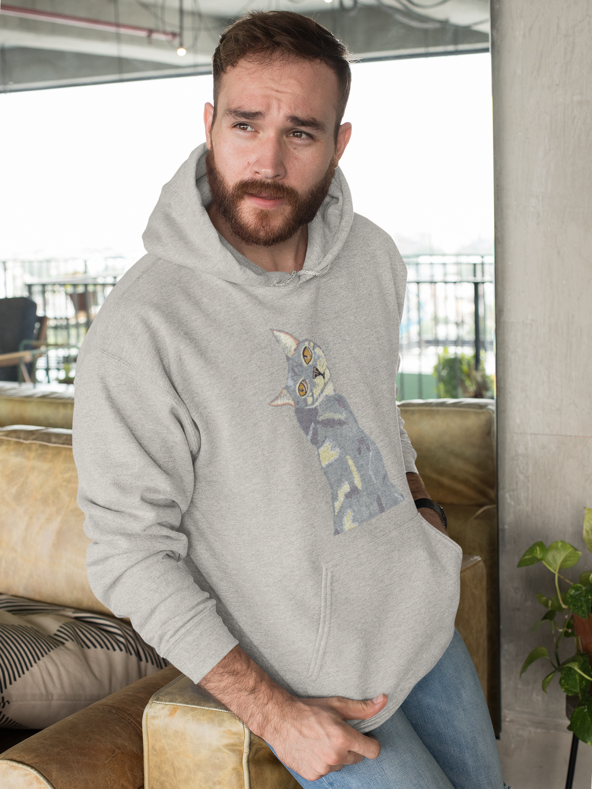 Bearded man leaning forward over a sofa, wearing the Mr. Grey Cat Portrait Hoodie in carbon grey.