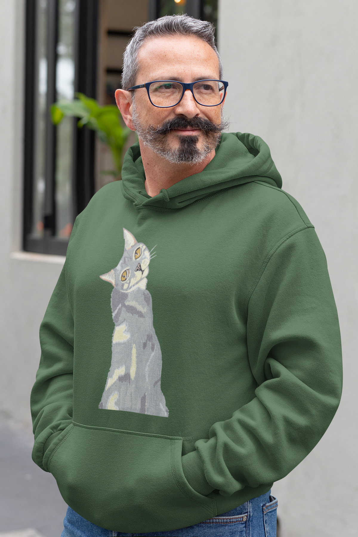 Man with a mustache and glasses standing outdoors, wearing the Mr. Grey Cat Portrait Hoodie in forest green.