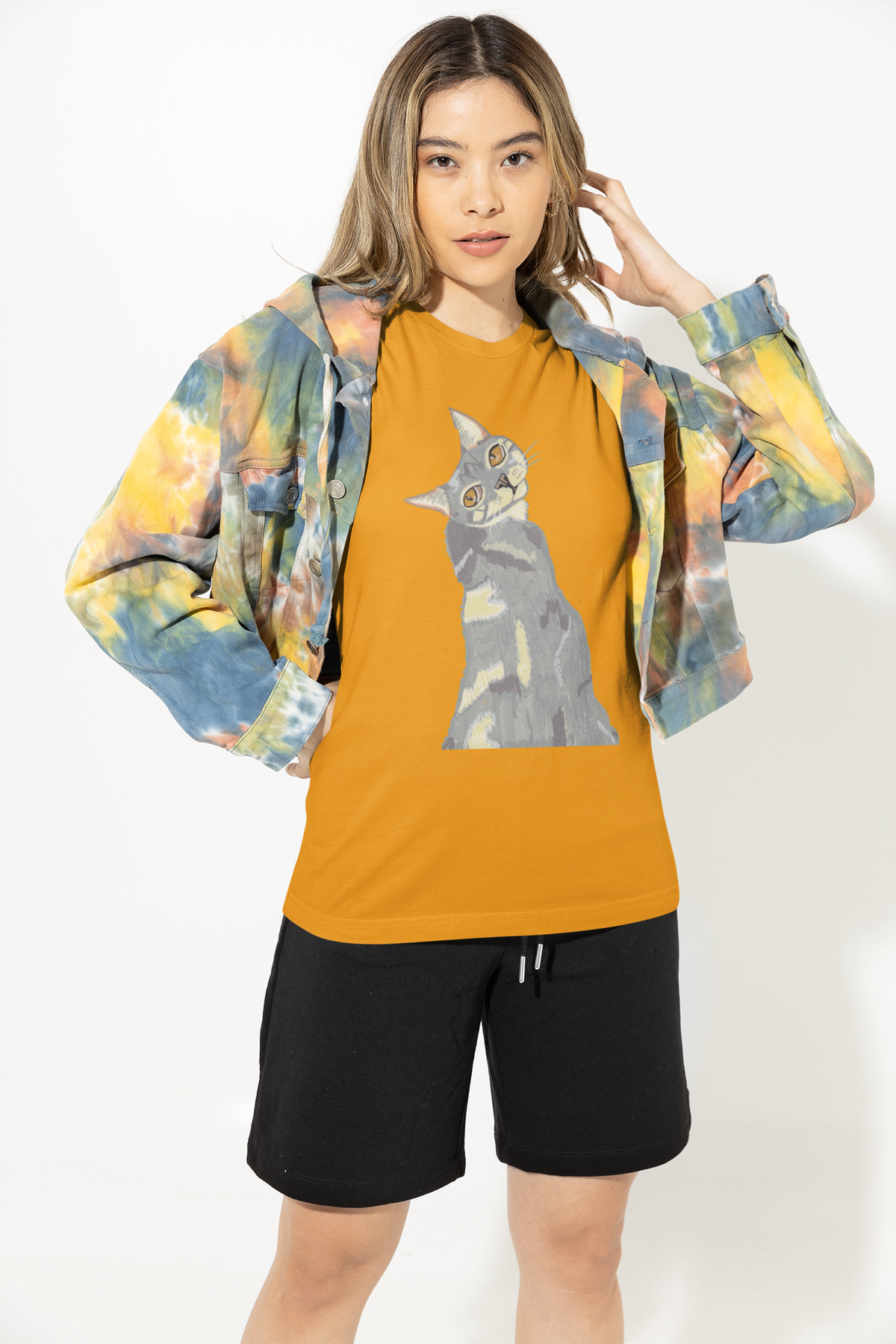 Woman in a colorful tie-dye jacket and black shorts wearing the Mr. Grey Cat Portrait T-Shirt in gold.