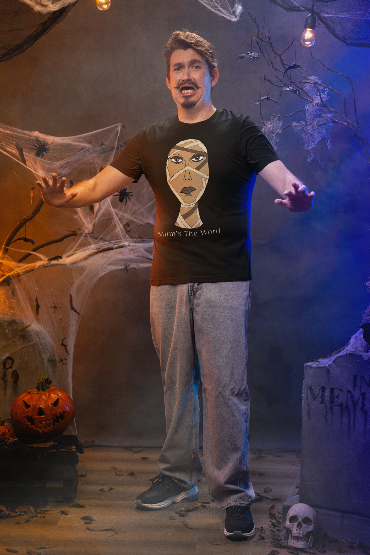 Worried man standing in a haunted house set wearing a black heather t-shirt with the mummy face and Mum’s The Word text