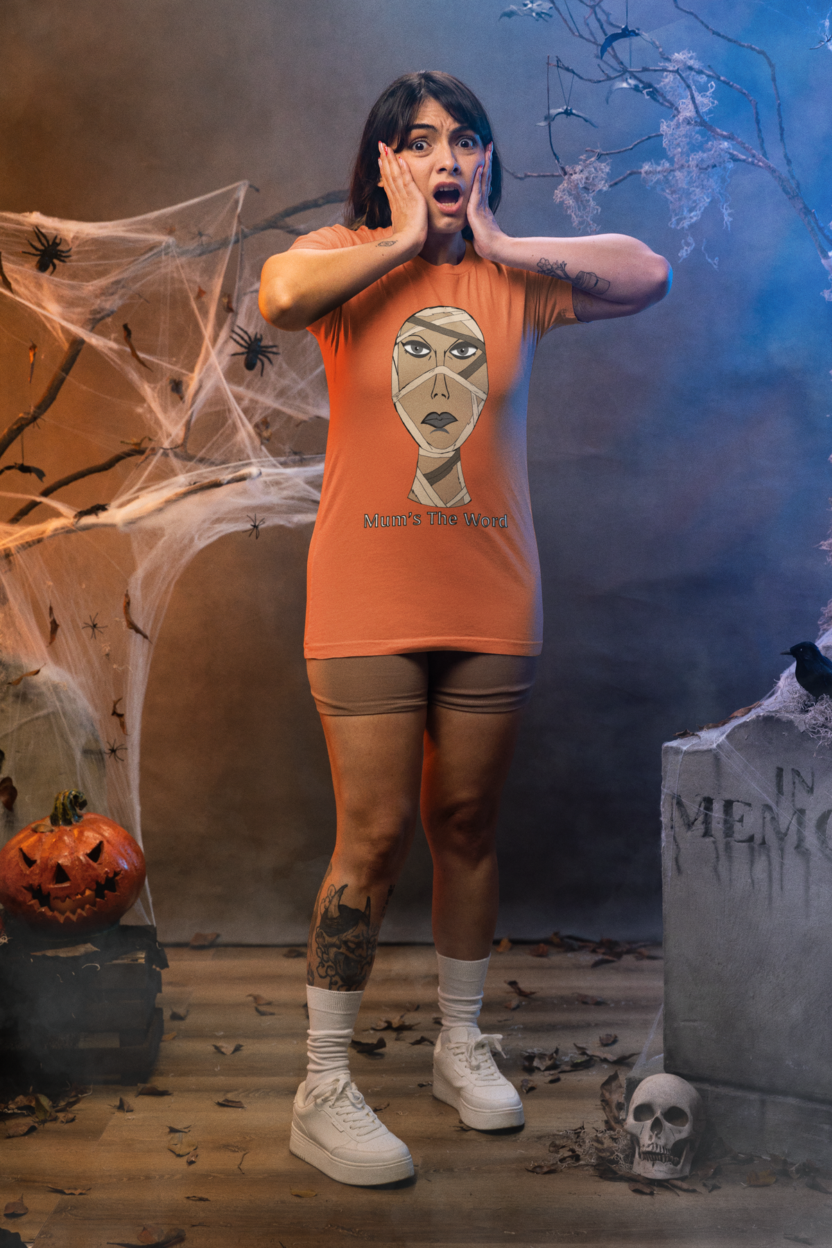 Woman with hands on her cheeks in a burnt orange t-shirt in a haunted house, mummy face and Mum’s The Word design