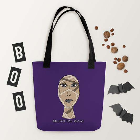 Purple tote bag with black straps held by a hand against a black background, featuring the wrapped mummy face and Mum’s The Word text