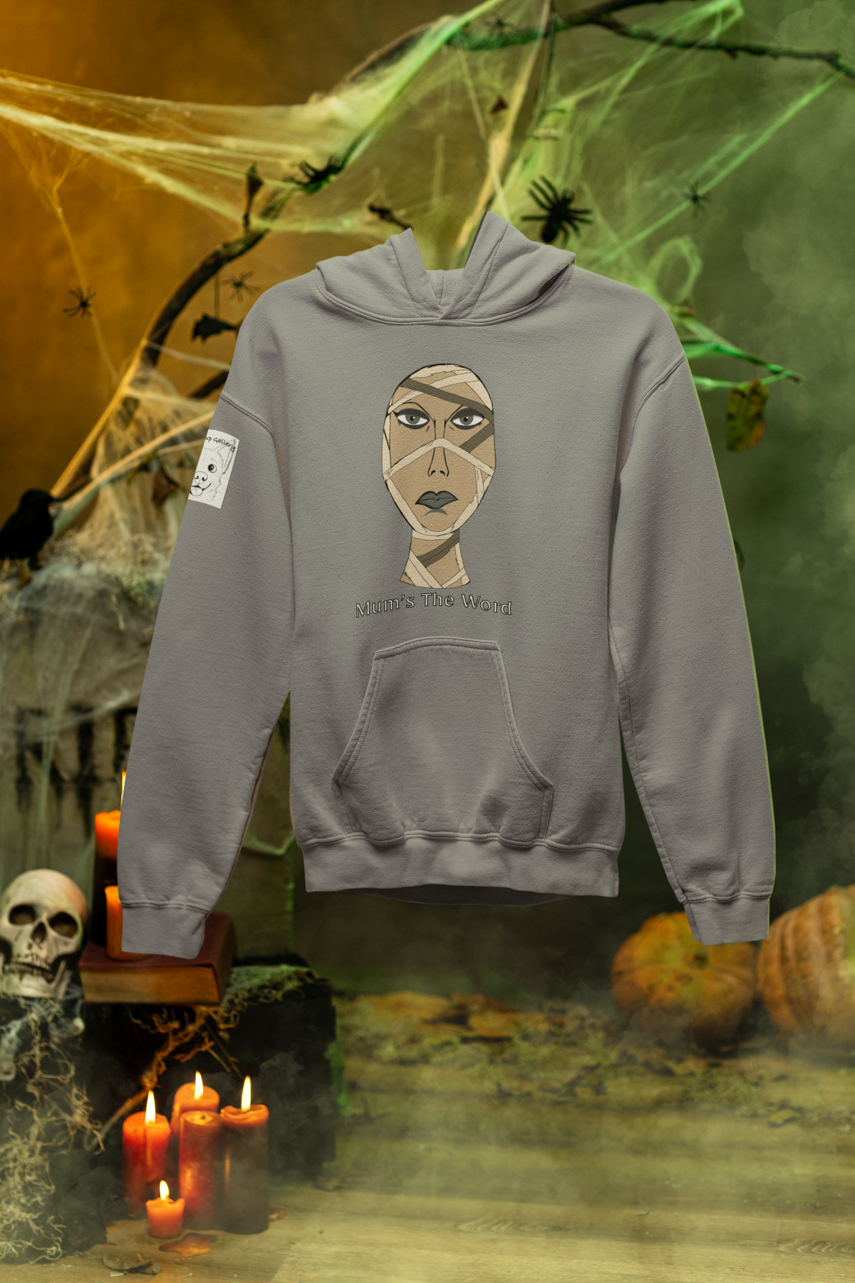 Sport grey hoodie hanging in a haunted set with candles, skull, and cobwebs, showing the mummy face and Mum’s The Word design