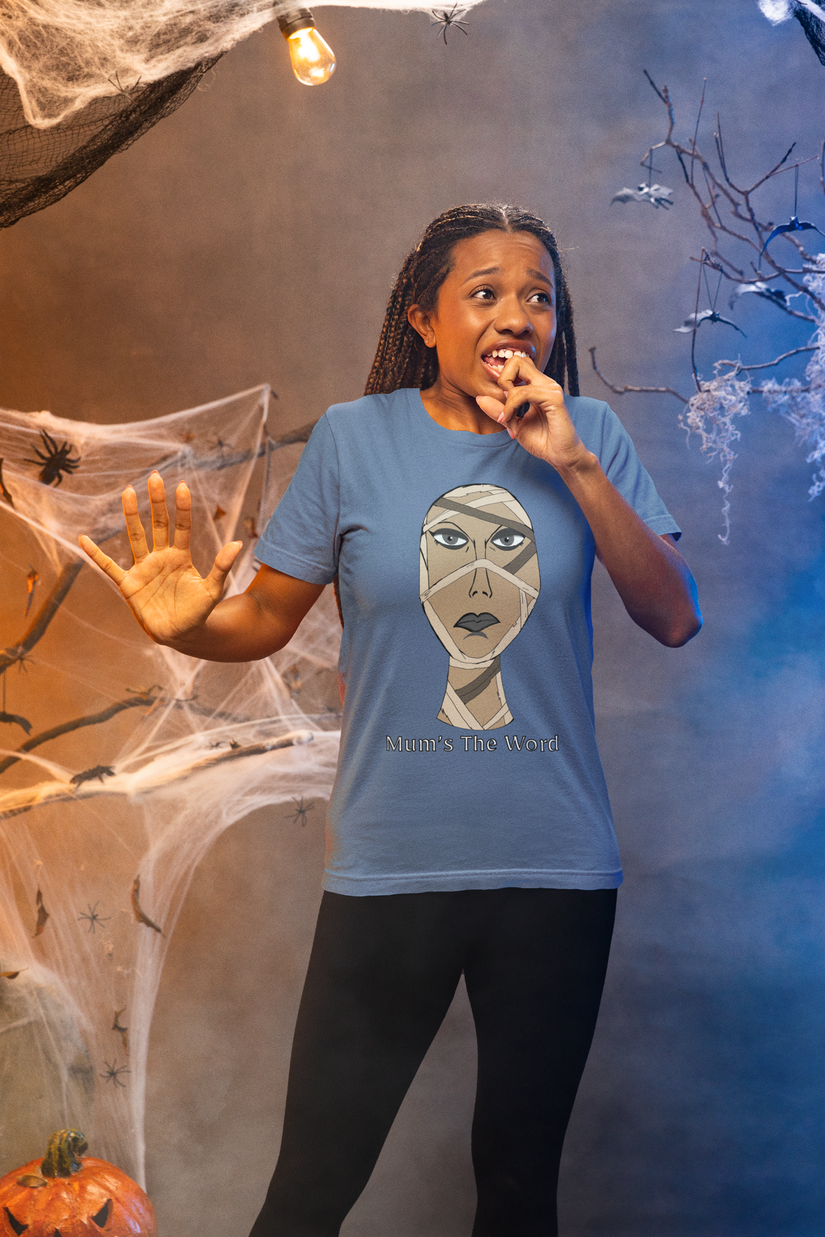 Fearful woman in a steel blue t-shirt standing in a cobwebbed haunted house, mummy face and Mum’s The Word print on the chest