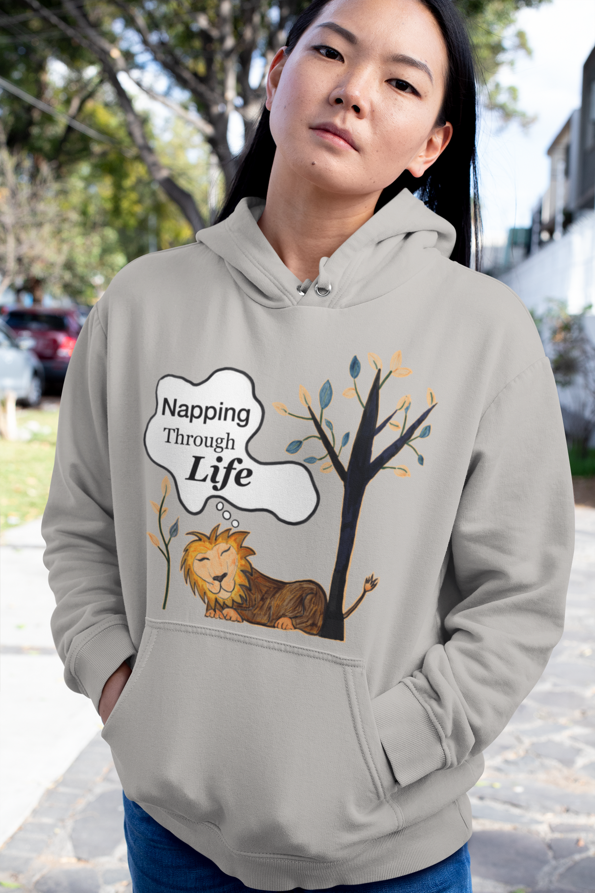 Carbon Grey hoodie with the Napping Through Life lion and tree design. Clean outdoor street shot, quiet confidence.
