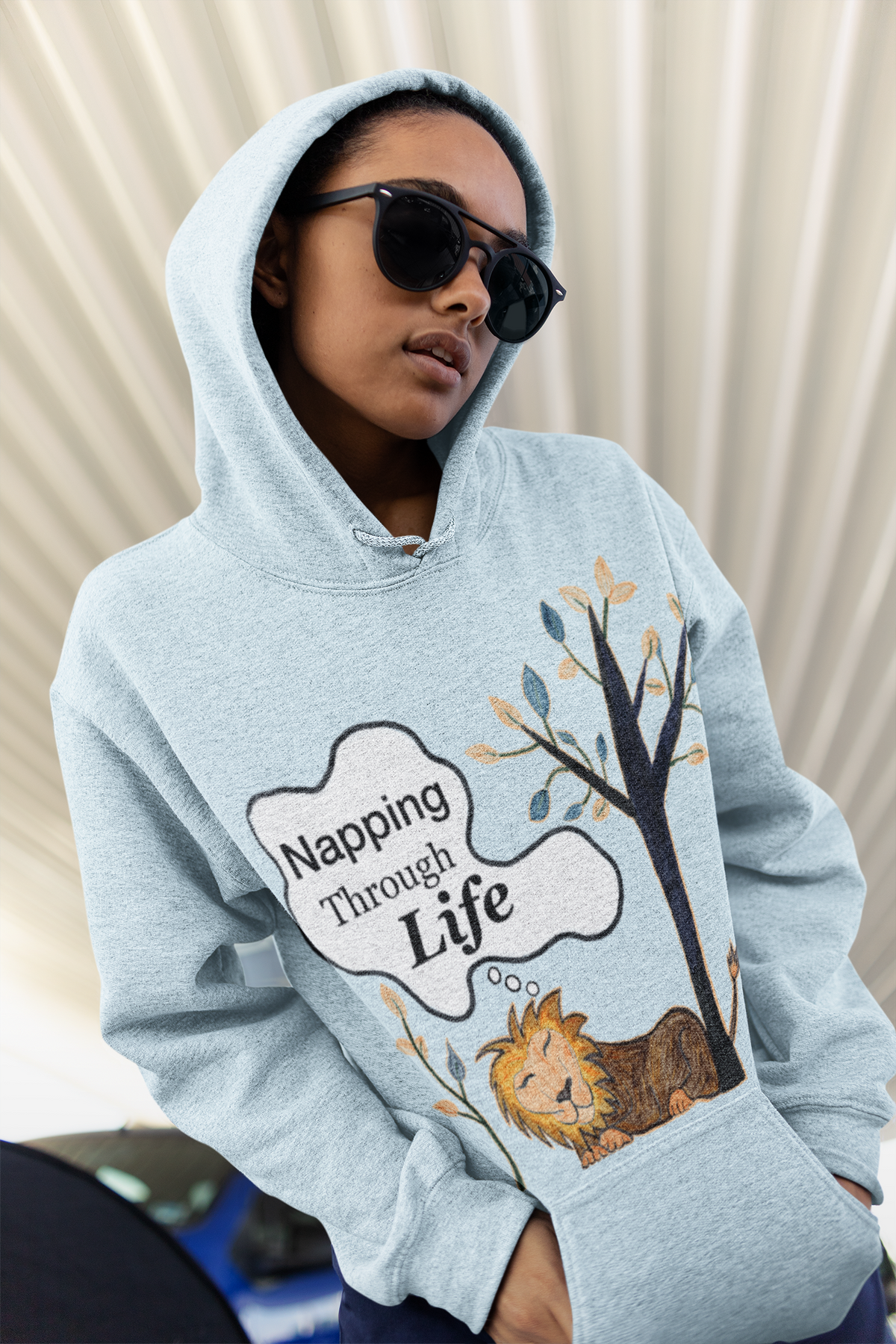 Soft Sky Blue hoodie, hood up, Napping Through Life print front and center. Cool, low-key vibe with sunglasses.