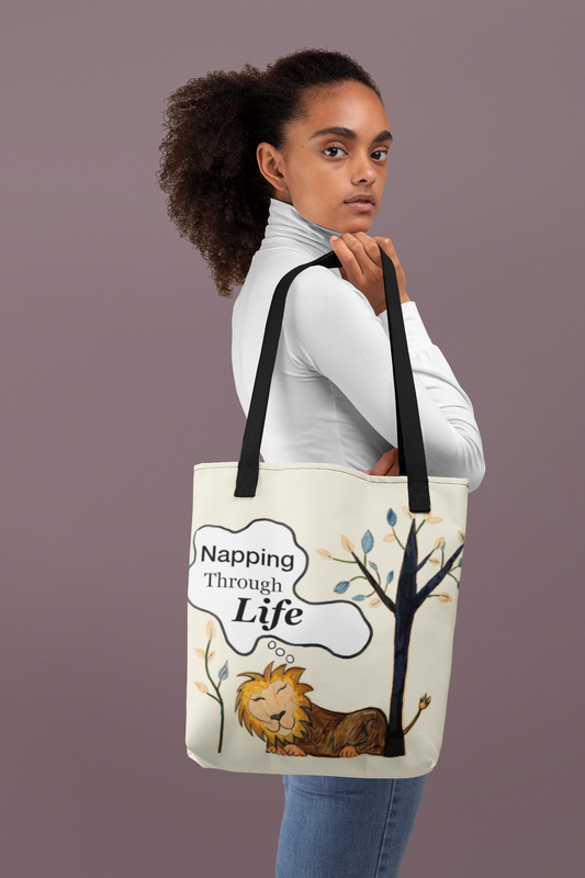 Cream tote with black straps featuring the Napping Through Life design. Model in white turtleneck holding the bag against a solid mauve background.
