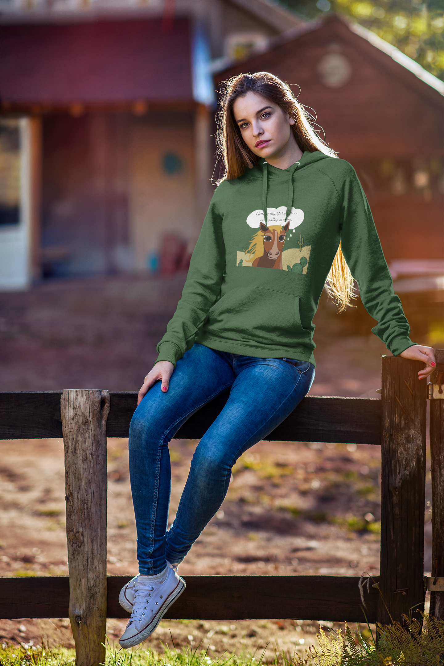 Woman sitting on wooden fence wearing forest green One Gallop at a Time hoodie with horse design