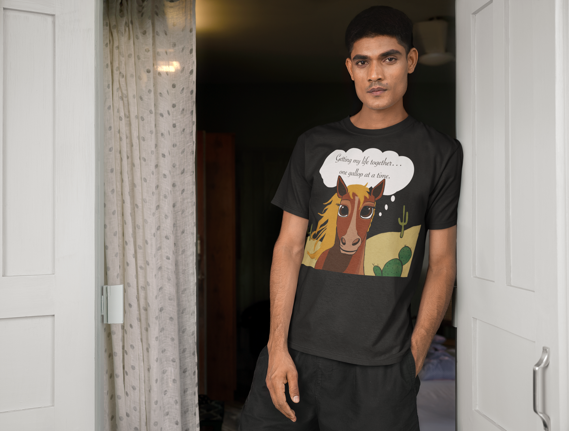 Man leaning in doorway wearing black One Gallop at a Time t-shirt