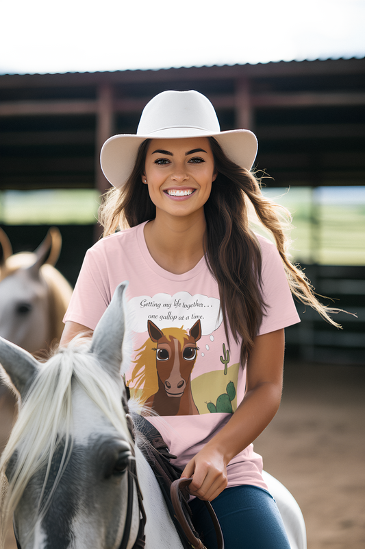 Smiling woman wearing cowboy hat and light pink One Gallop at a Time t-shirt while sitting on a horse