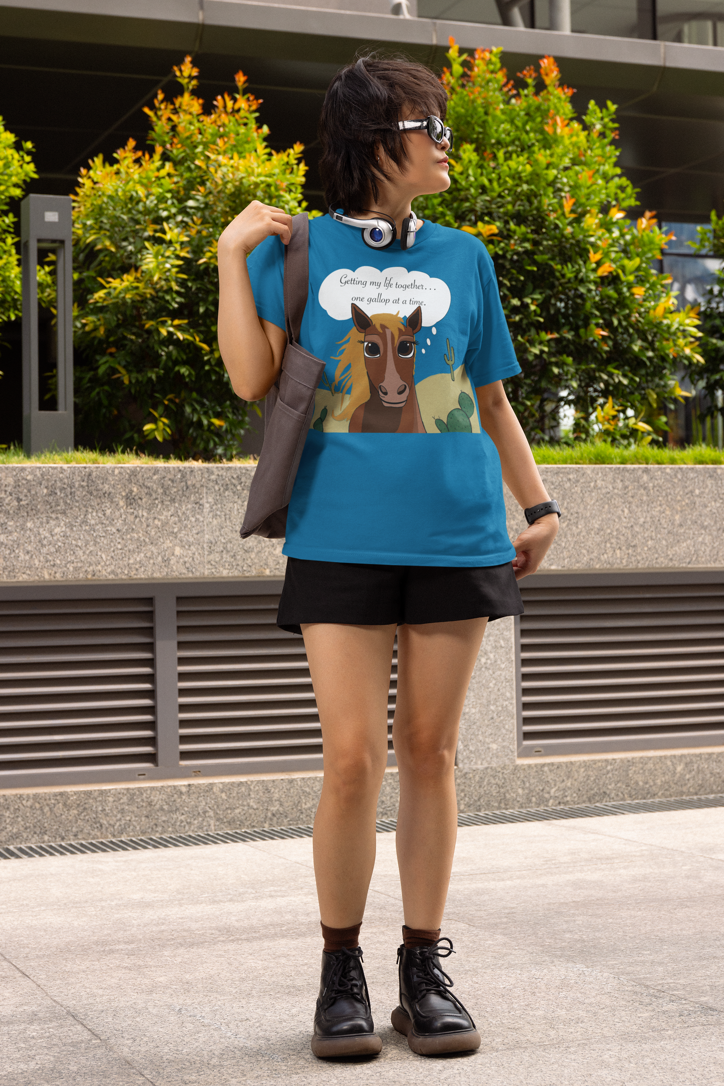 Woman wearing headphones and sunglasses with sapphire blue One Gallop at a Time t-shirt outdoors