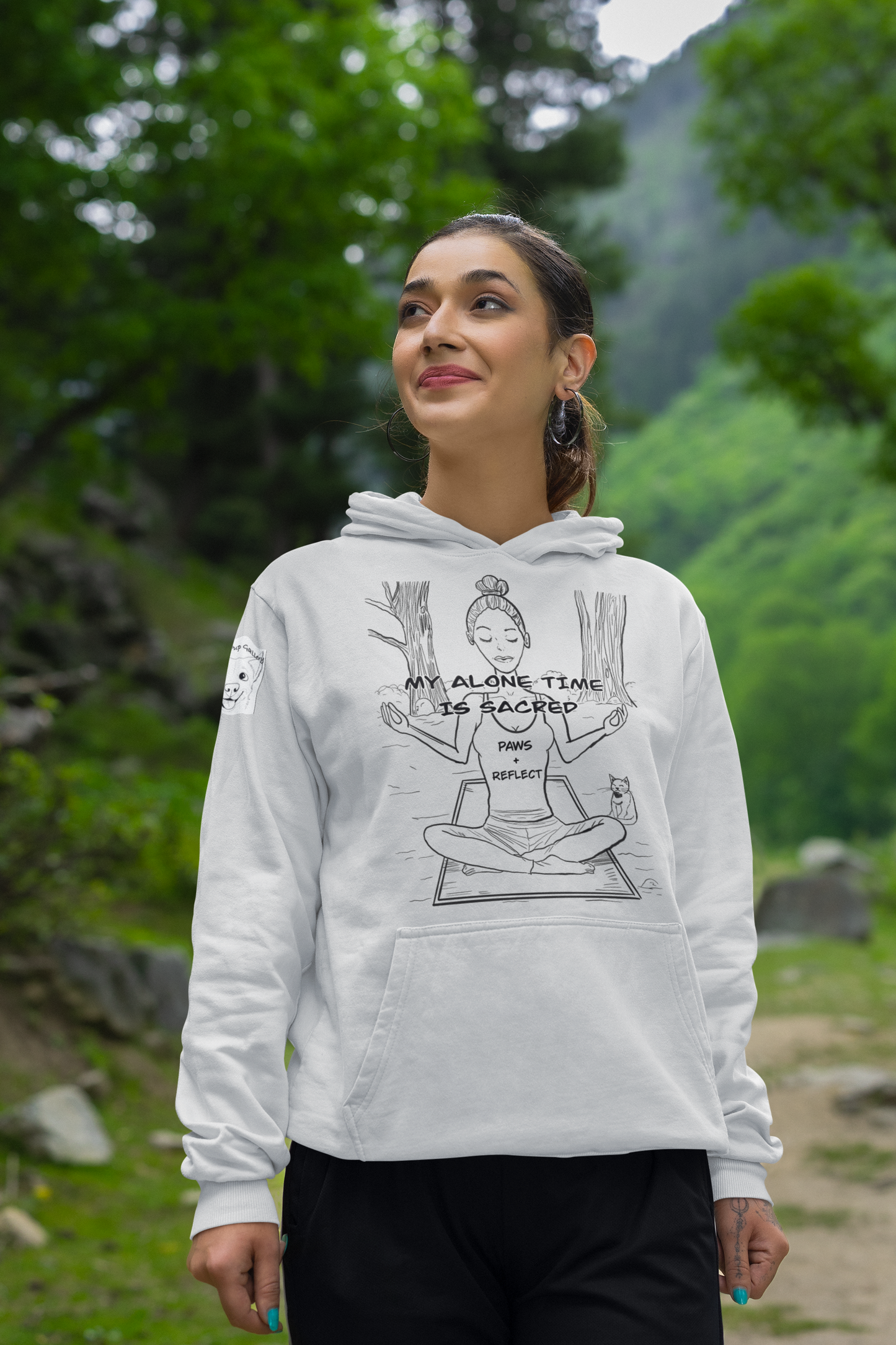 Woman standing on a mountain trail wearing an ash grey Gildan hoodie with the bold black “My Alone Time is Sacred” Paws & Reflect yoga design, looking upward in nature