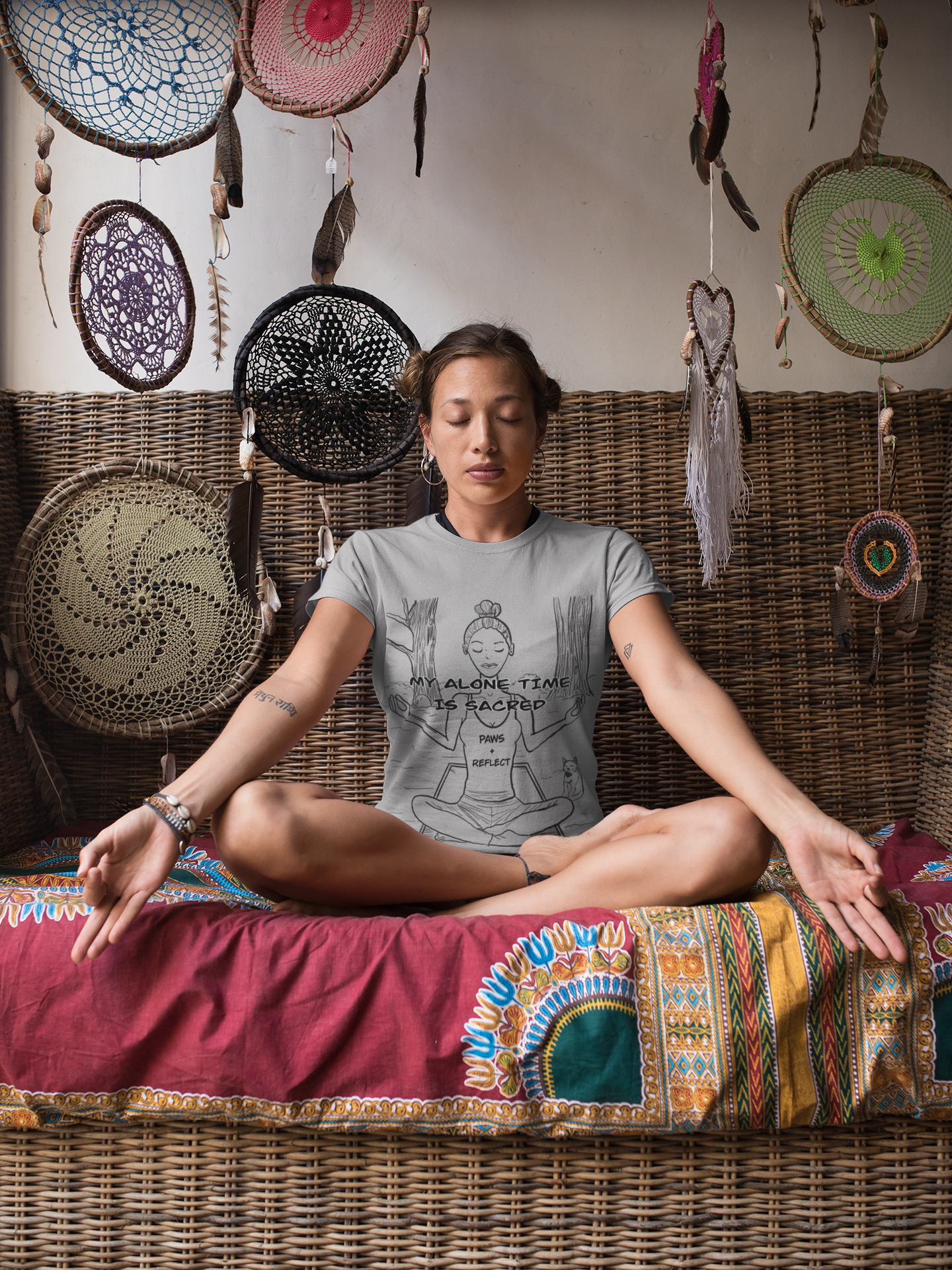 Woman sitting in a meditative yoga pose on a patterned cushion wearing an RS Sport Grey t-shirt with the darker “My Alone Time is Sacred” Paws & Reflect design, surrounded by dreamcatchers and tribal ornaments