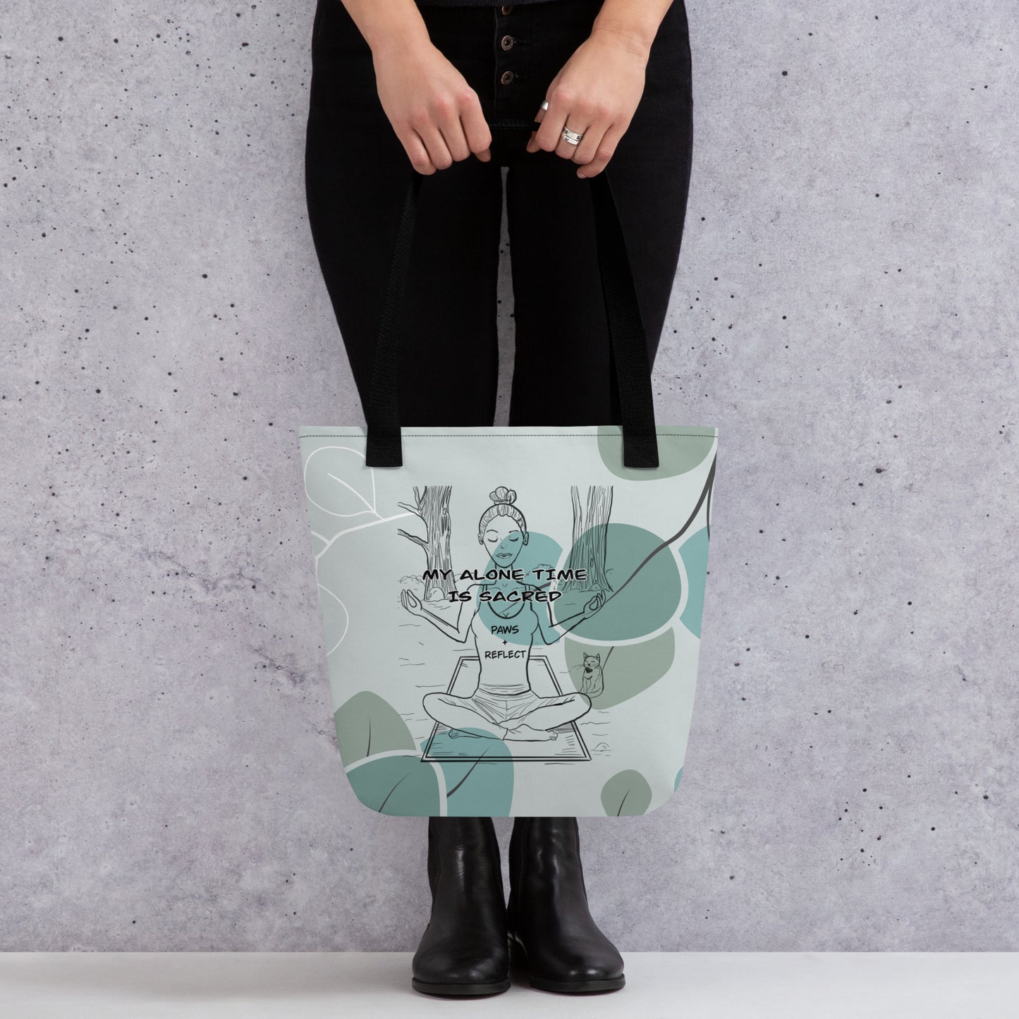 Person holding the sage green eucalyptus all-over print tote bag featuring the bold “My Alone Time is Sacred” Paws & Reflect design, shown from the front against a concrete wall