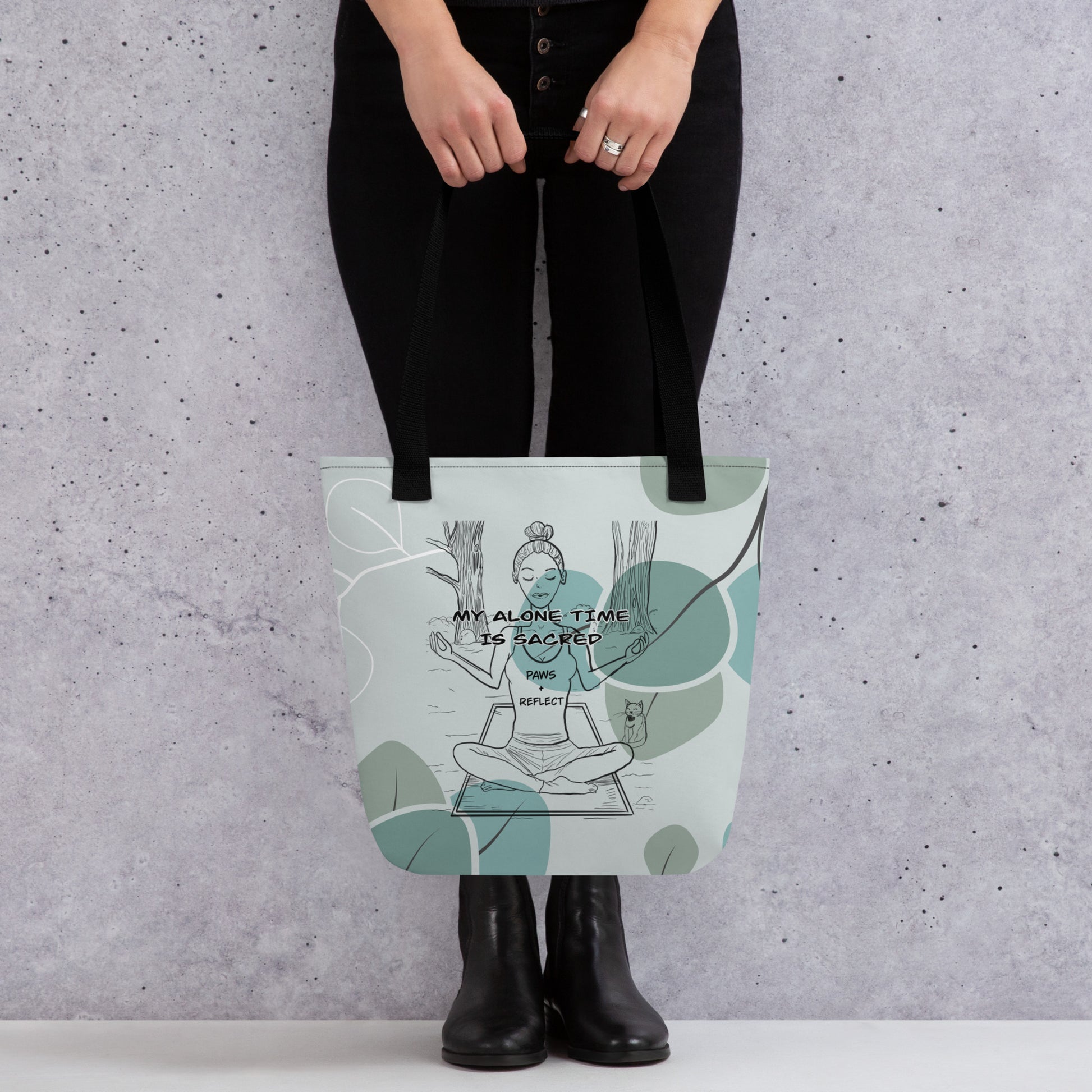 Person holding the sage green eucalyptus all-over print tote bag featuring the bold “My Alone Time is Sacred” Paws & Reflect design, shown from the front against a concrete wall