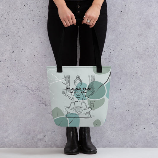 Person holding the sage green eucalyptus all-over print tote bag featuring the bold “My Alone Time is Sacred” Paws & Reflect design, shown from the front against a concrete wall