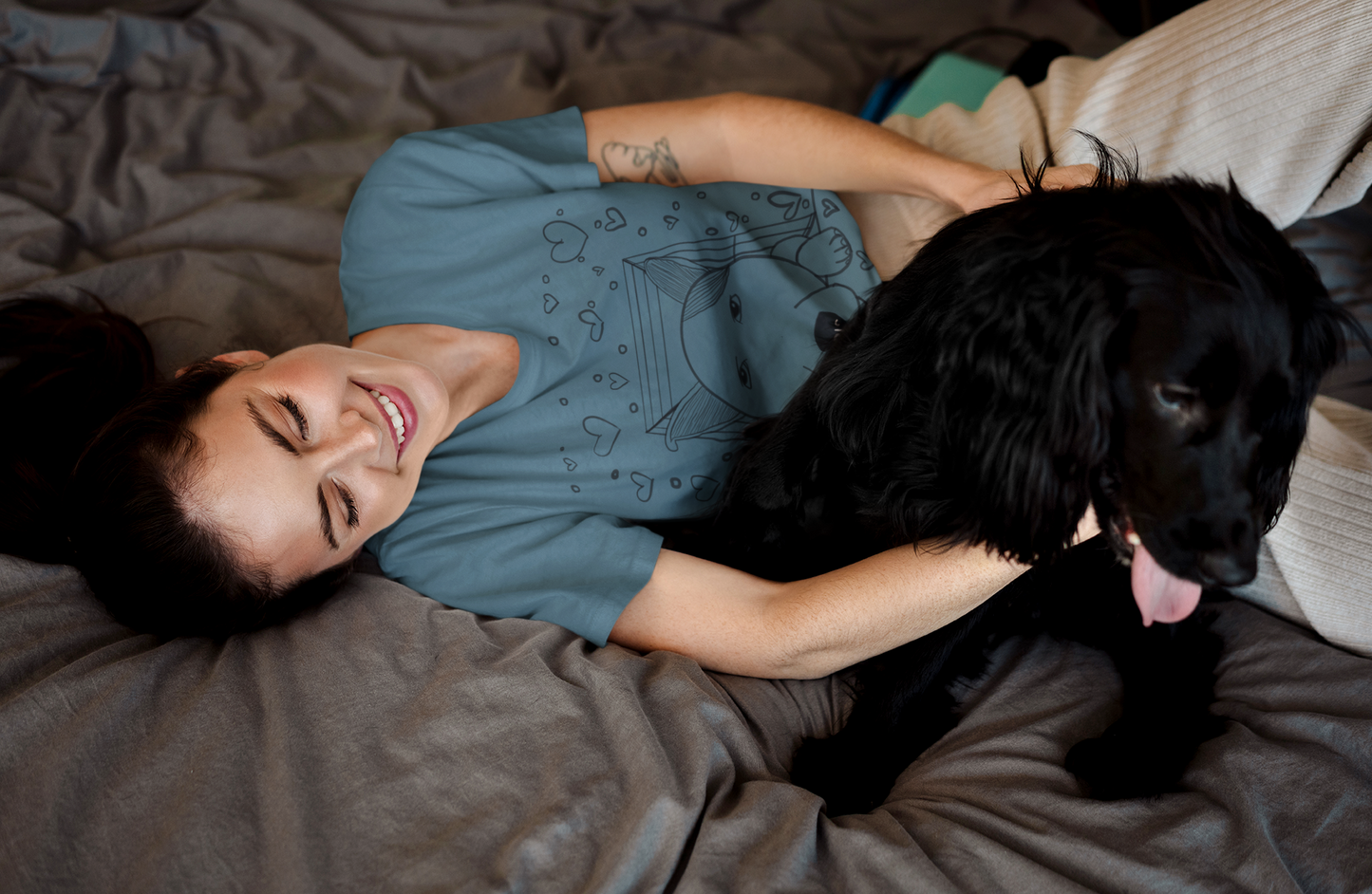 Woman cuddling with black dog in bed wearing heather deep teal "Pup Love" t-shirt with dog in box and hearts design – GrungePup Vet Chaos cute pet lover apparel