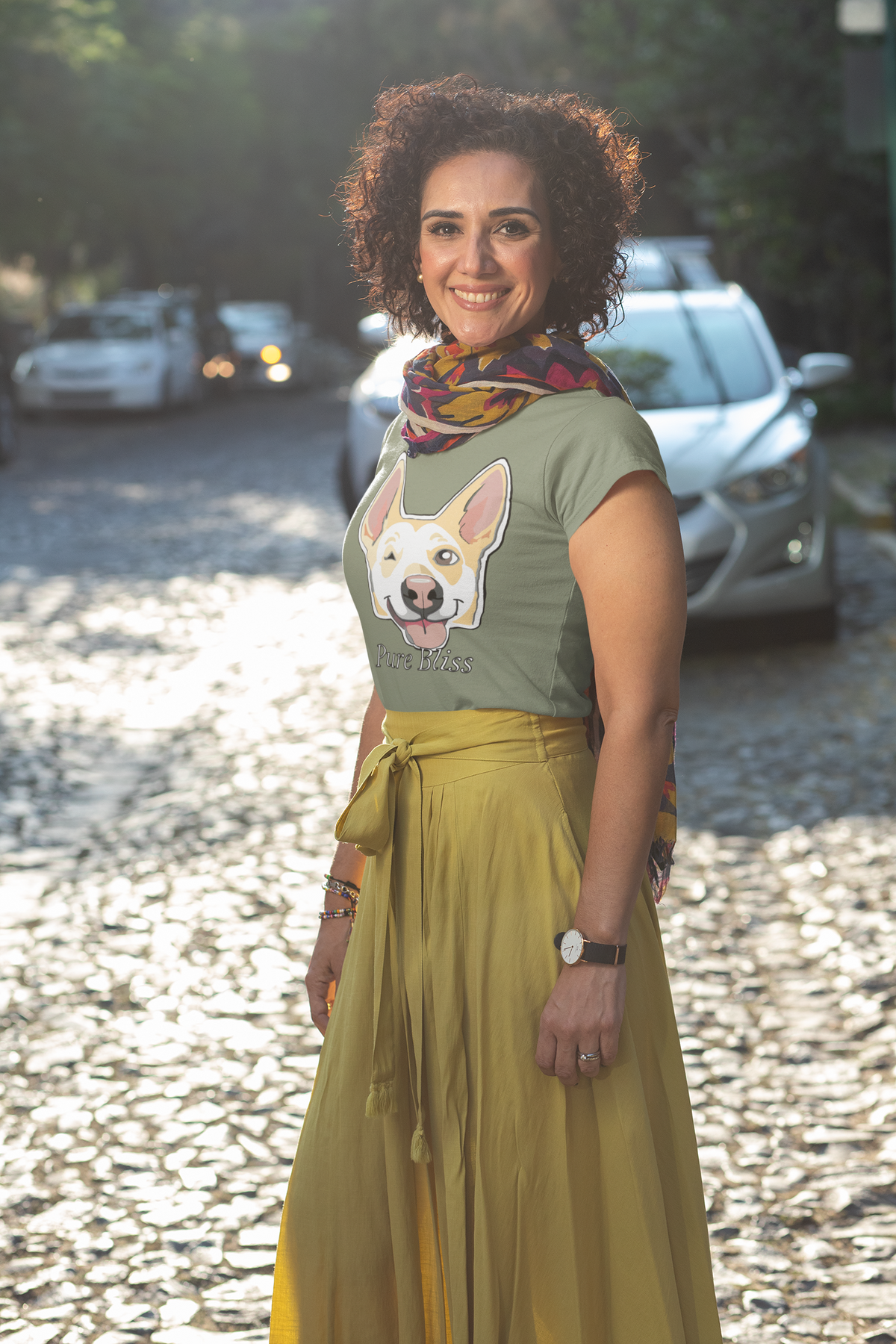 Woman in a military green Pure Bliss t-shirt, yellow skirt, and scarf standing on a cobblestone street. Nico Inspired by GrungePup Gallery.