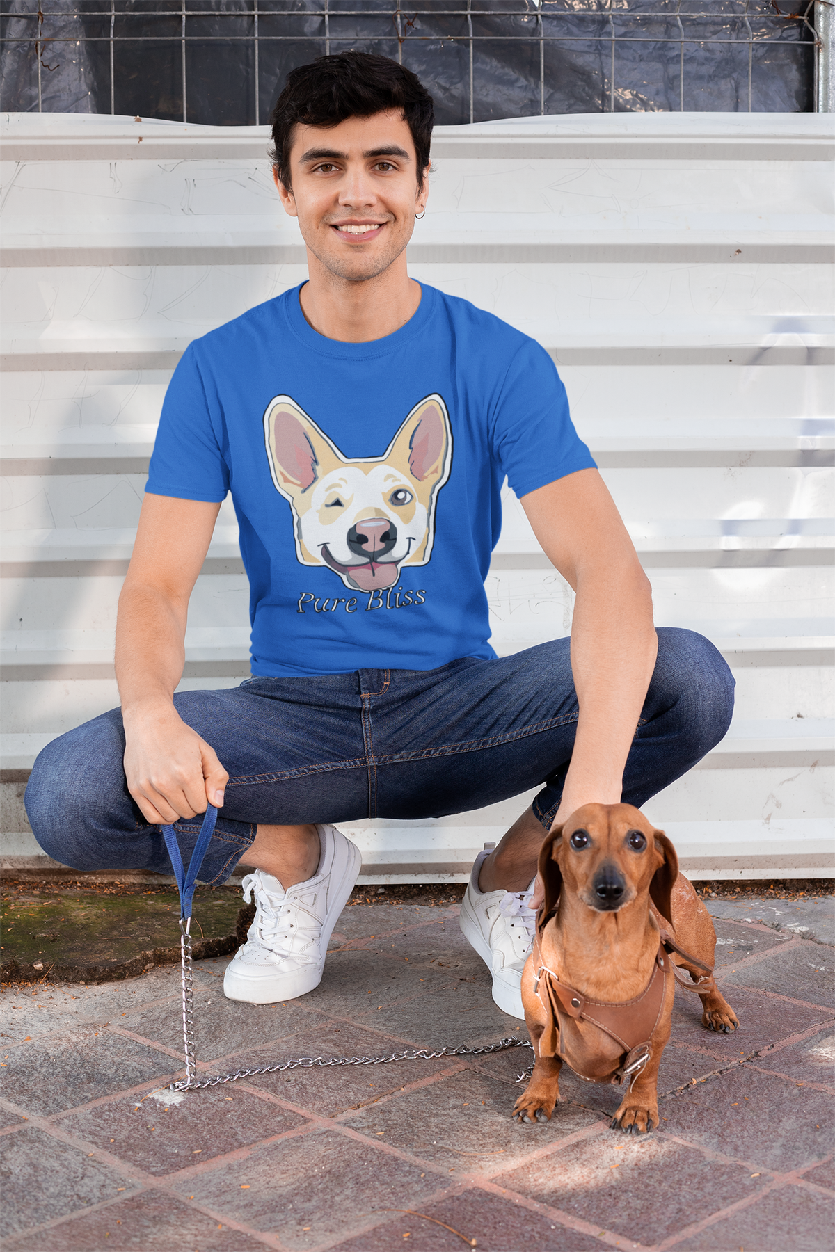 Man crouched next to a brown dachshund in a royal blue Pure Bliss t-shirt. Nico Inspired by GrungePup Gallery.