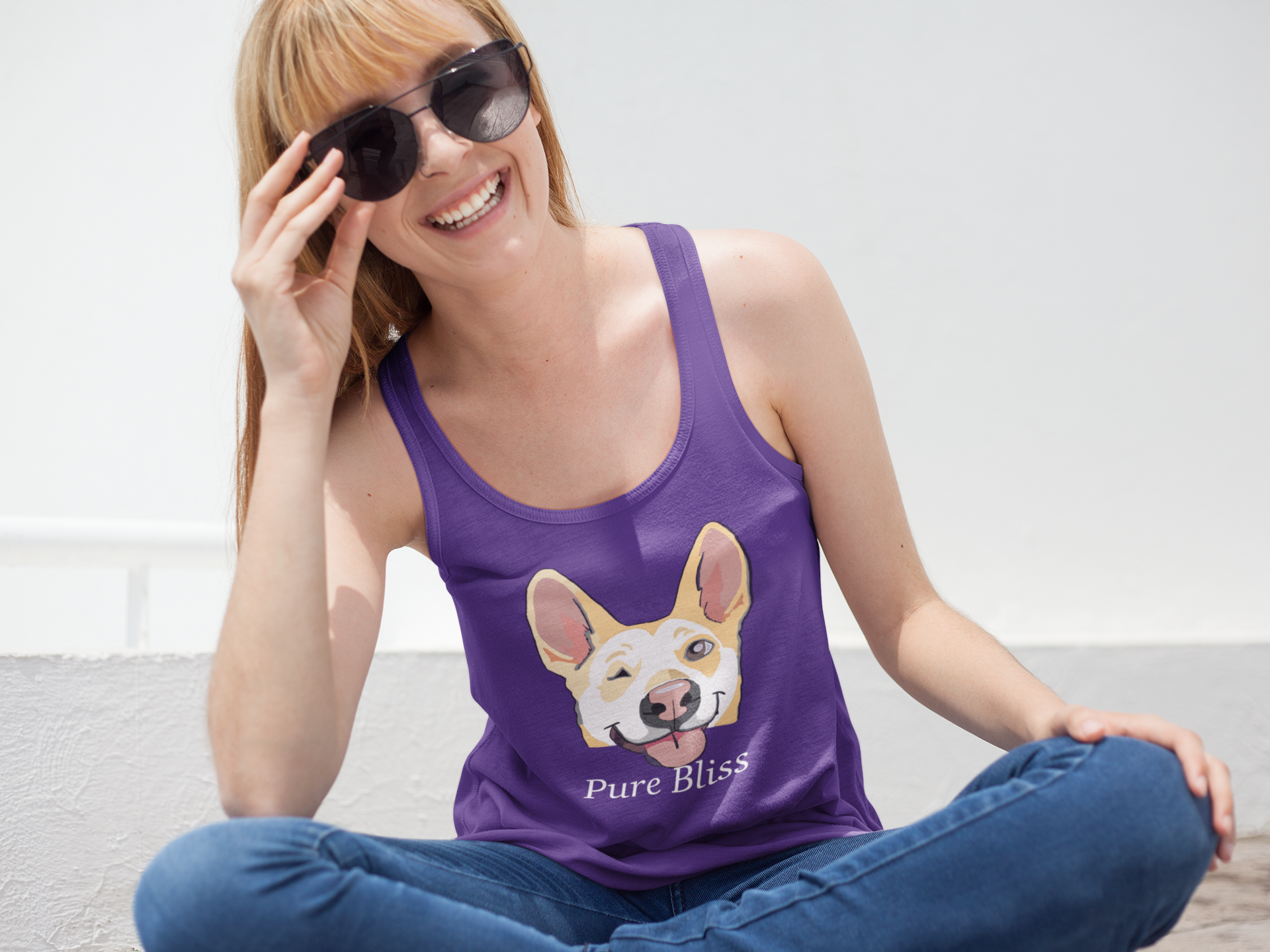 Woman with sunglasses sitting and smiling wearing purple Pure Bliss Nico Face racerback tank top