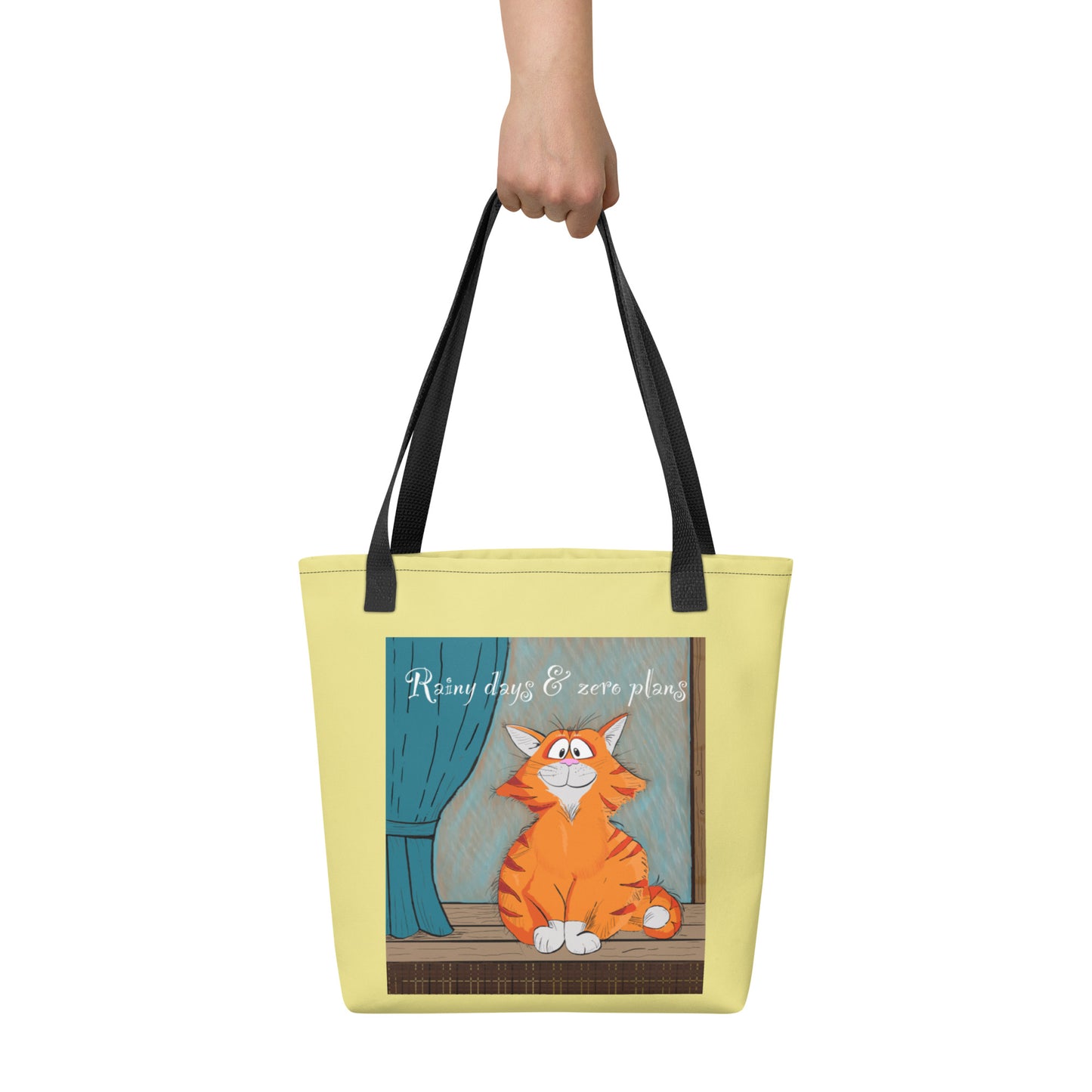 Hand holding Rainy Days & Zero Plans cat tote bag with orange cat design and text "Rainy days & zero plans"