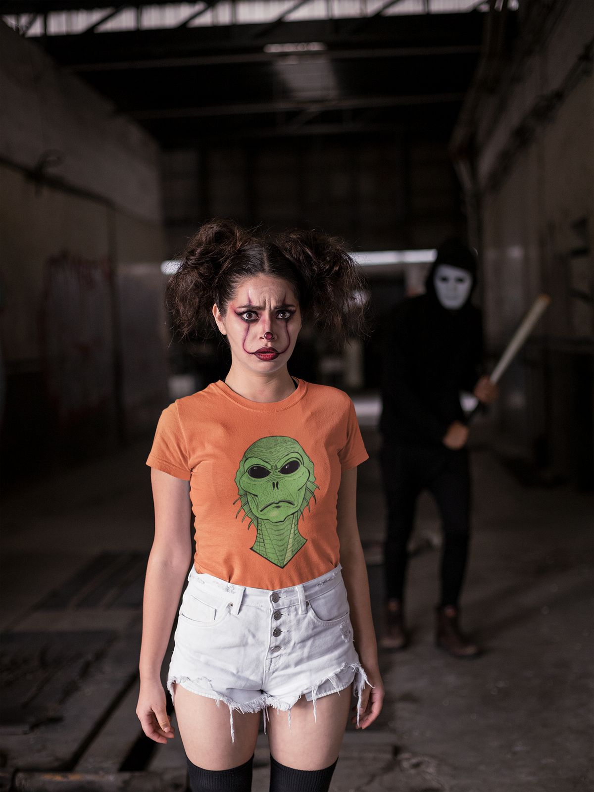 Woman with a scared expression in an orange t-shirt standing in a warehouse, Swamp Thang face on the chest
