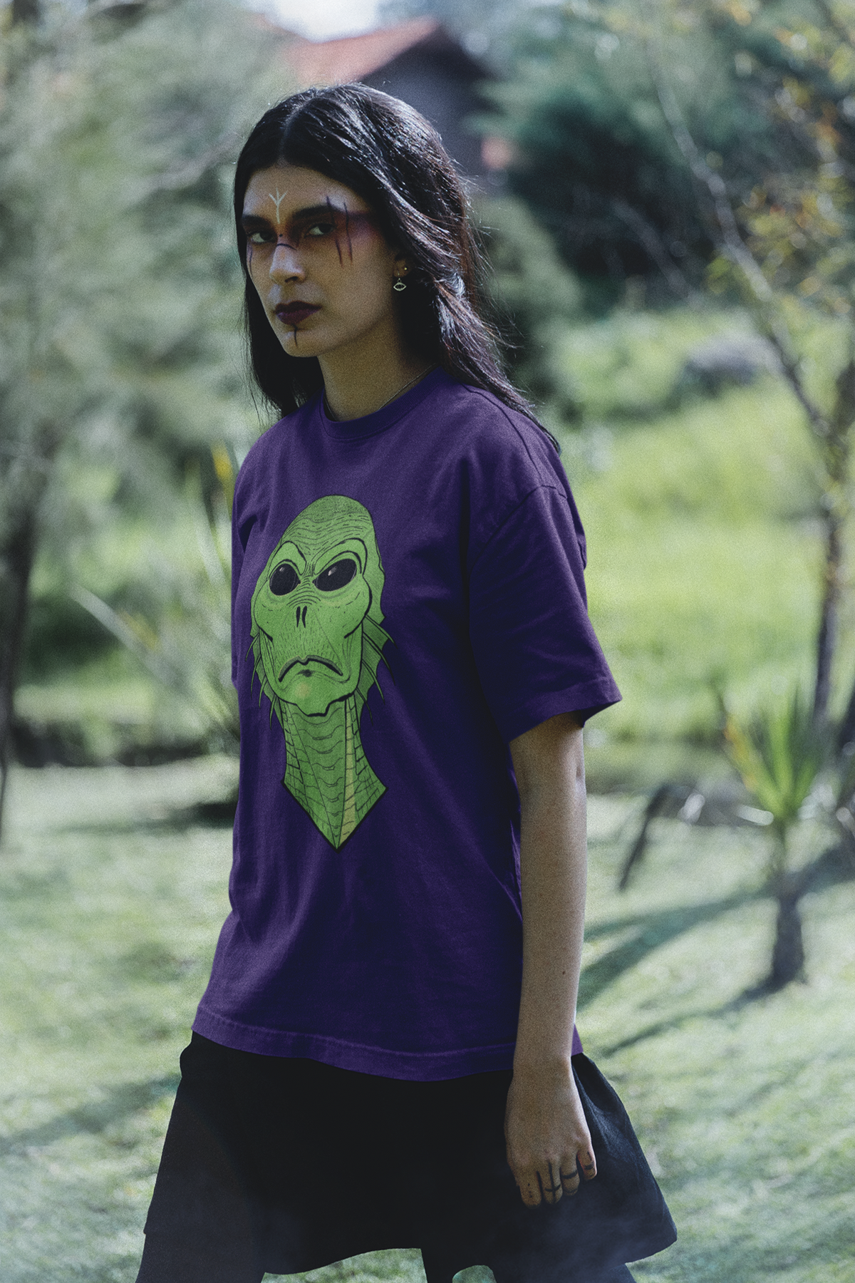 Woman with dark forest-inspired makeup standing outside in a team purple t-shirt with the Swamp Thang face