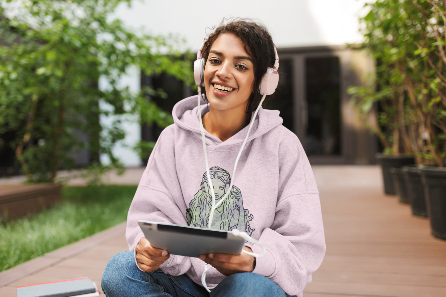 Lady sitting and listening to music wearing light pink Gildan hoodie with That Girl, Alice grunge-cute Wonderland design. Edgy and whimsical self-taught art for the ones who fell down the rabbit hole with style.