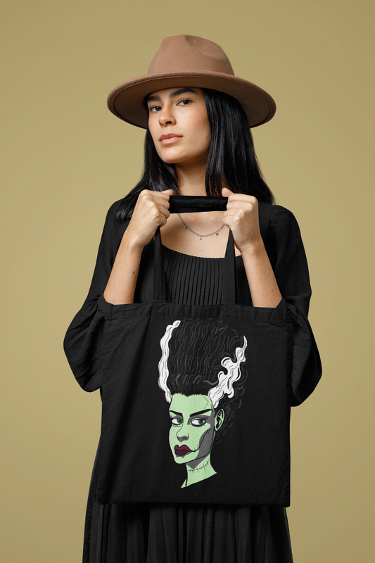 Woman in a brown hat holding a black tote bag with The Bride portrait on the front. GrungePup Gallery.