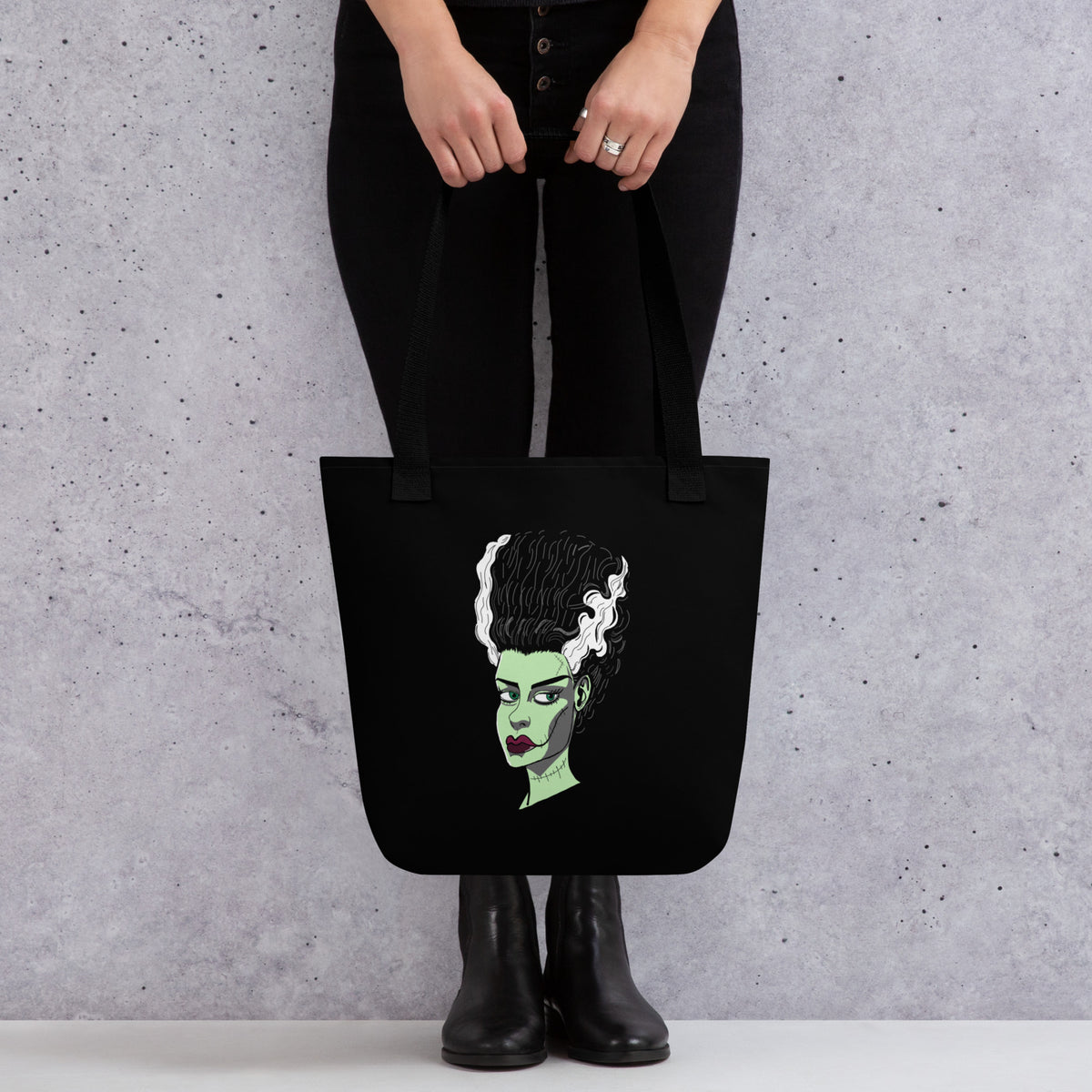 Black tote bag with The Bride face print held in front of a person, shown from the waist down. GrungePup Gallery.