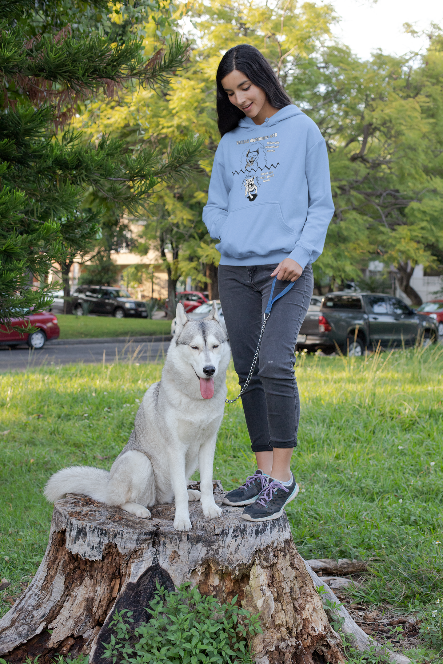 Woman standing in a park with a husky wearing a carolina blue Gildan 18500 hoodie featuring the full Vet Tech Nightmare #18 split design.