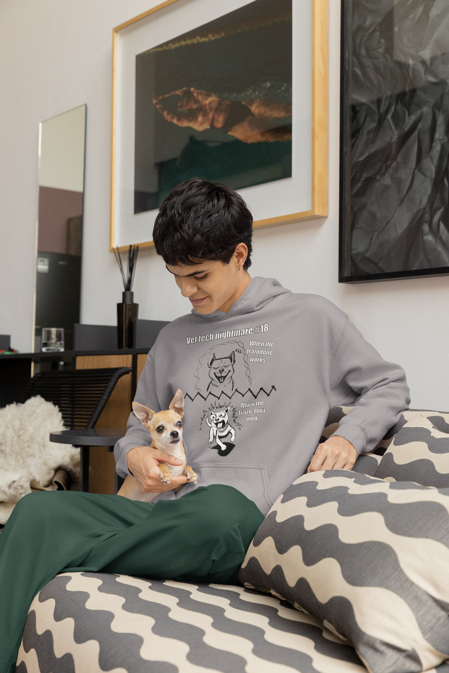 Man sitting indoors wearing a sport grey Gildan 18500 hoodie with the Vet Tech Nightmare #18 design, holding a small chihuahua.