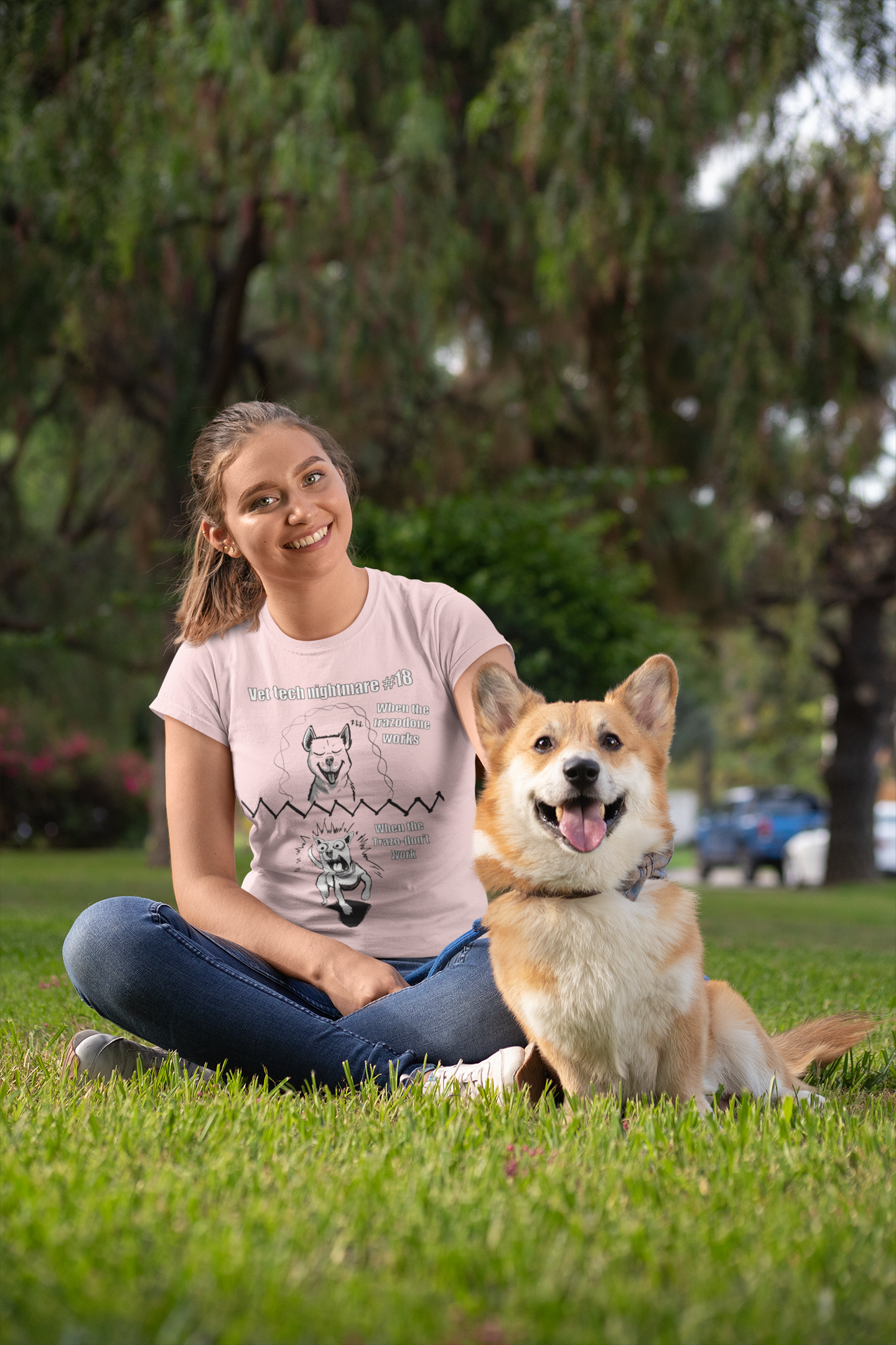 Smiling woman sitting on grass with a happy corgi wearing a light pink Gildan 5000 t-shirt displaying Vet Tech Nightmare #18 with the happy dog panel and demonic dog panel.