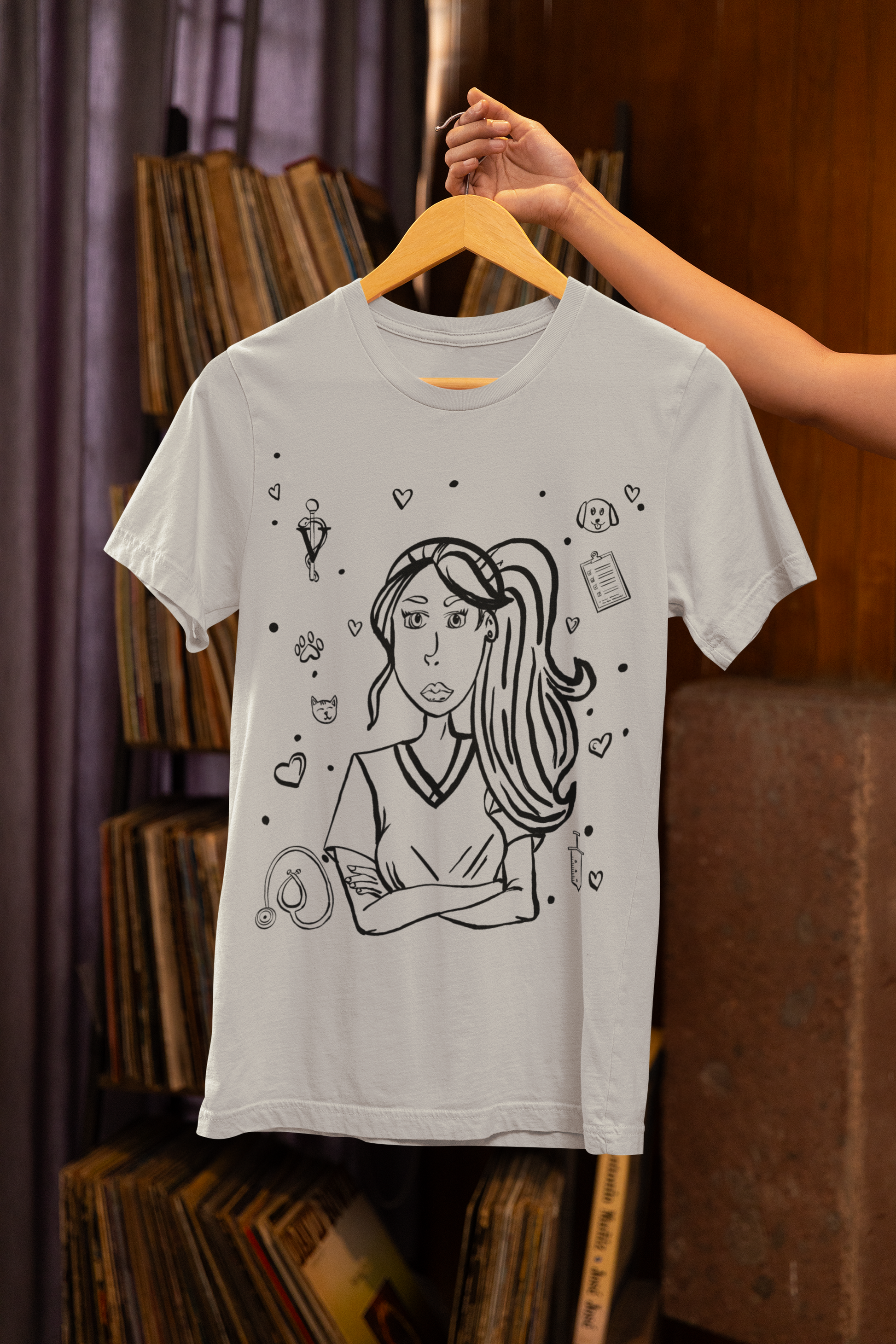 Athletic heather Vet Vibe t-shirt hanging on a wooden hanger against a vinyl record shop background, showing the full darkened line-art vet girl design with hearts, stethoscope, and animal icons.