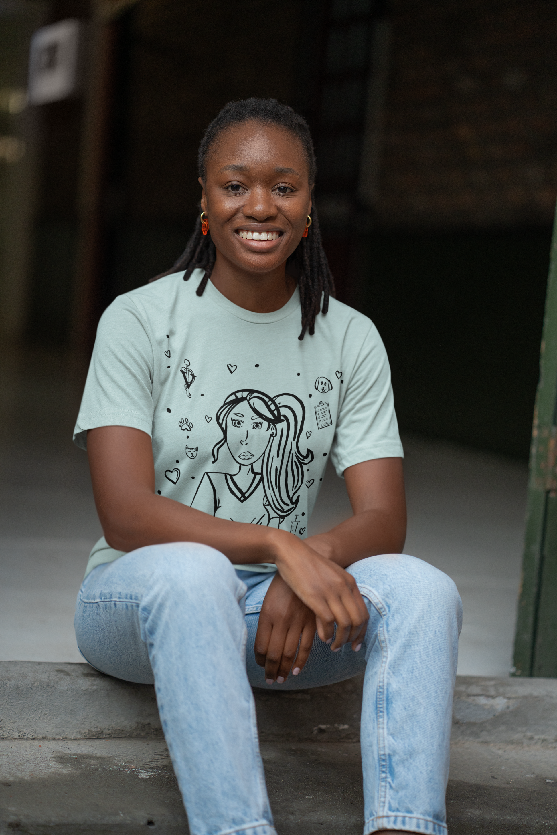Black woman with braided hair sitting on concrete steps smiling while wearing a heather prism blue Vet Vibe t-shirt with the darkened line-art vet girl design.
