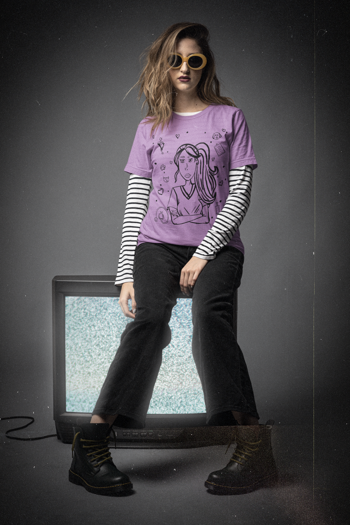 Woman with wavy hair and yellow sunglasses sitting on an old TV wearing a heather team purple Vet Vibe t-shirt with the darkened line-art vet girl design and layered striped sleeves.
