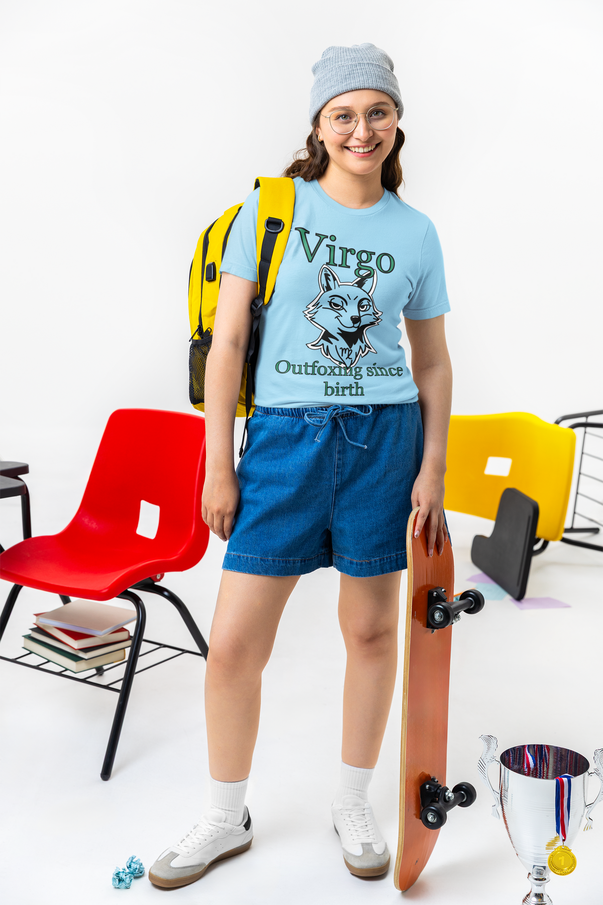Smiling woman in a beanie wearing an ocean blue Bella + Canvas Virgo Outfoxing Since Birth t-shirt in a classroom setting while holding a skateboard.