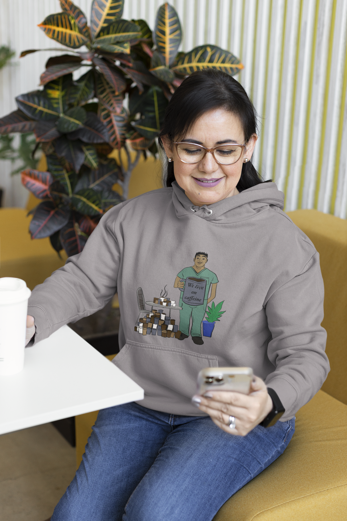 Woman on phone wearing sport grey "We Live on Caffeine" hoodie with coffee and vet tech illustration – GrungePup Vet Chaos relatable vet med apparel