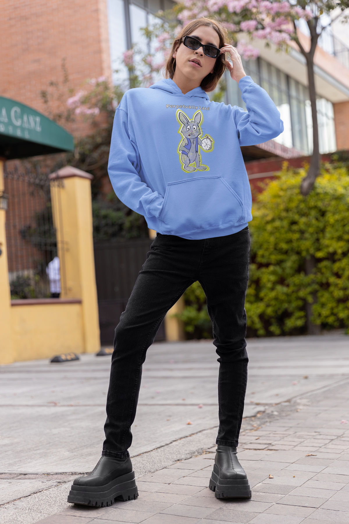 Person in sunglasses posing on a city sidewalk in a carolina blue White Rabbit Perpetually Late hoodie, black jeans, and platform boots. GrungePup That Girl, Alice.