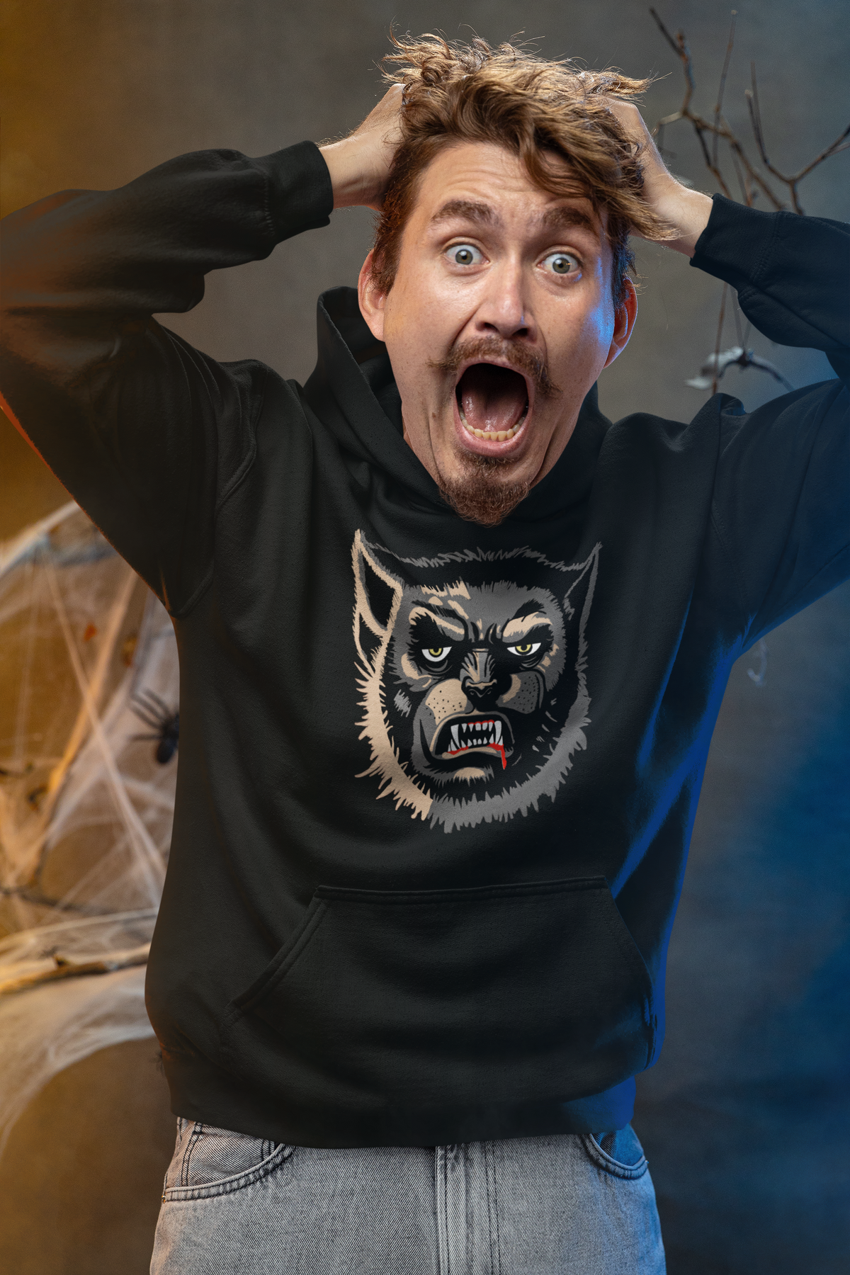 Man grabbing his hair and screaming in a Halloween studio, wearing a black Gildan Wolfman hoodie with the face-only Wolfman print