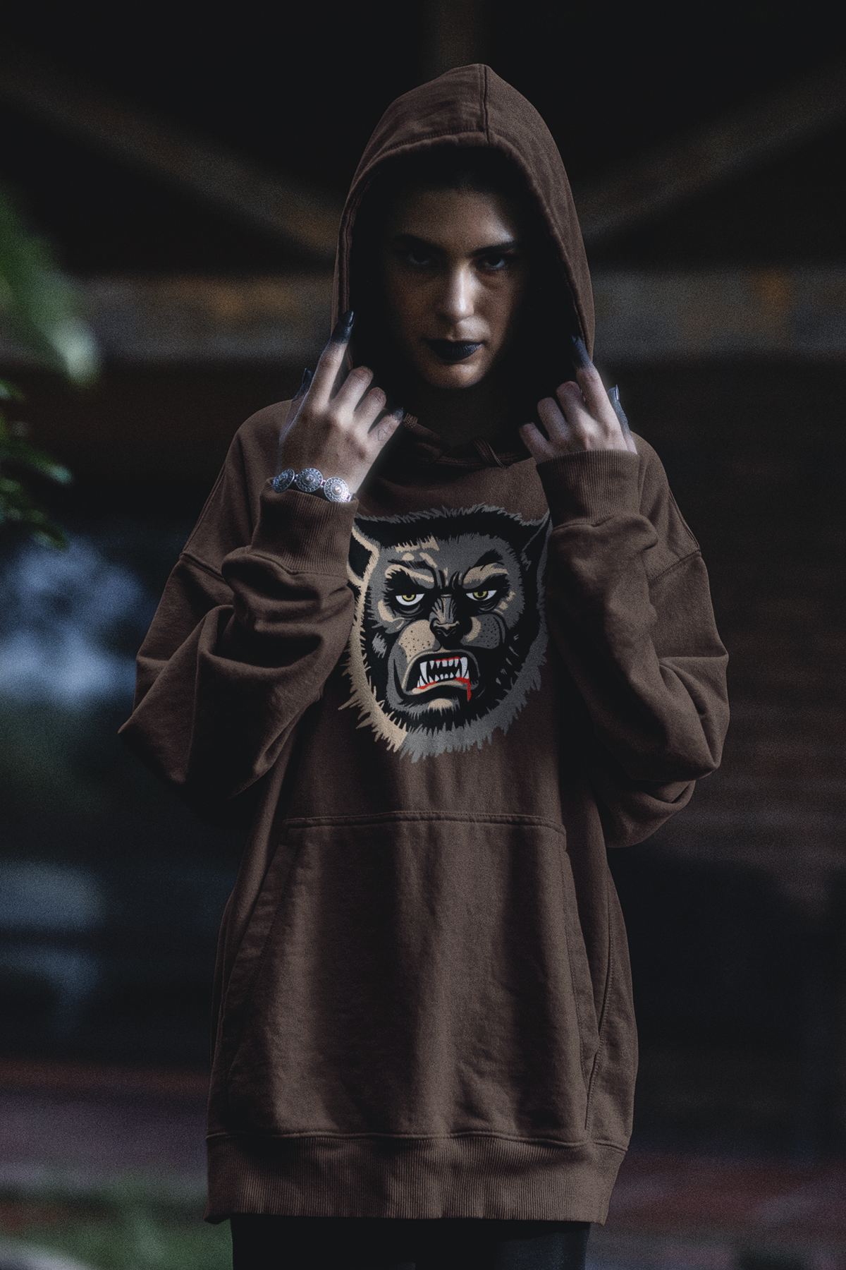 Woman with black lipstick and painted fingertips pulling up a dark chocolate Wolfman hoodie, face-only Wolfman print on the chest
