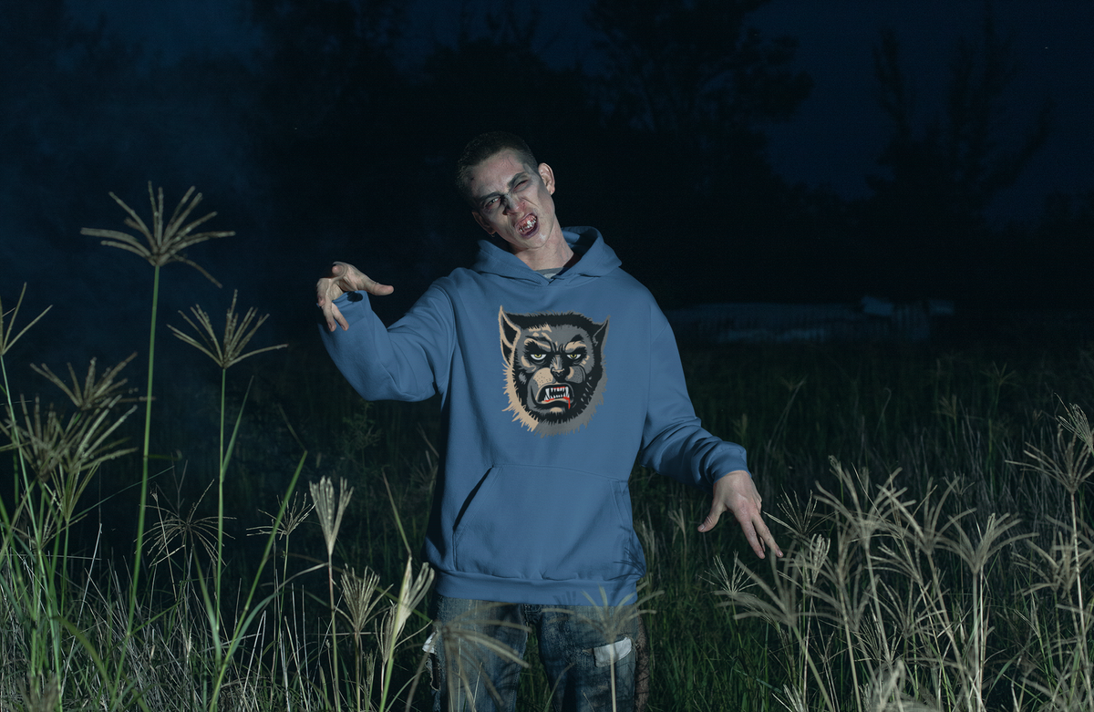 Man styled as a zombie standing in tall grass at night, wearing an indigo blue Wolfman hoodie with yellow eyes and a lip drip