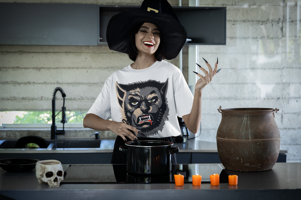 Smiling woman in a witch hat cooking in a kitchen, wearing a white Wolfman t-shirt with the yellow-eyed snarling Wolfman face print