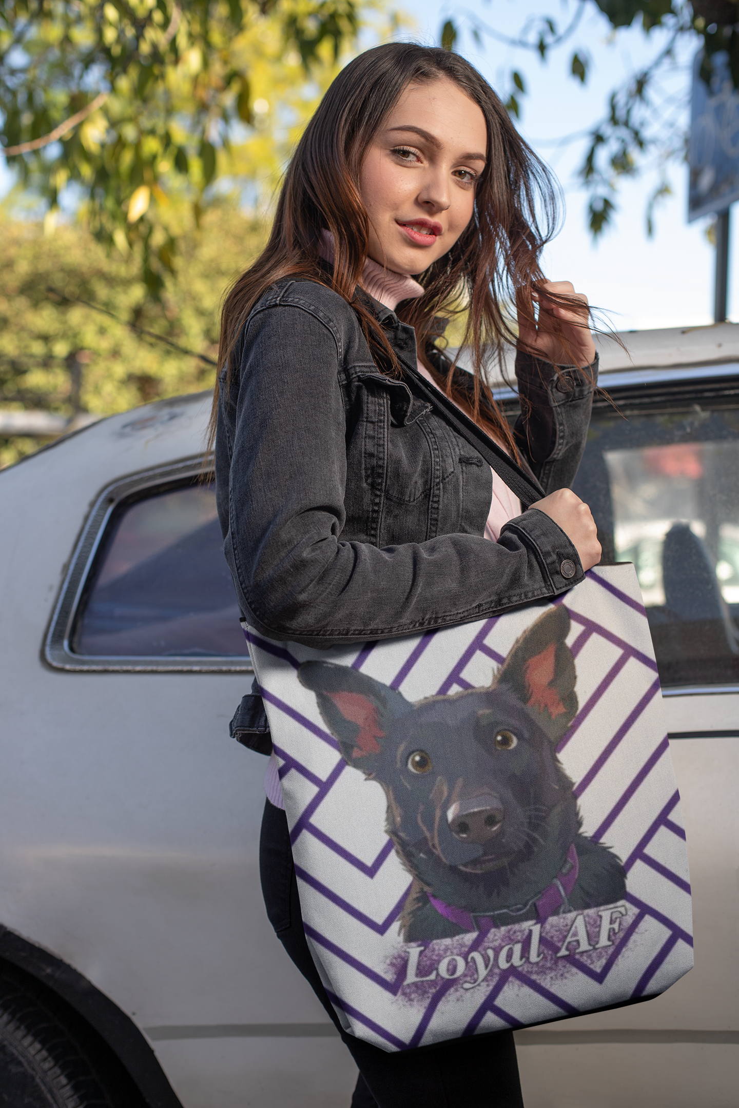 Woman standing in front of a car holding the Mathis Loyal AF all-over print tote bag by GrungePup
