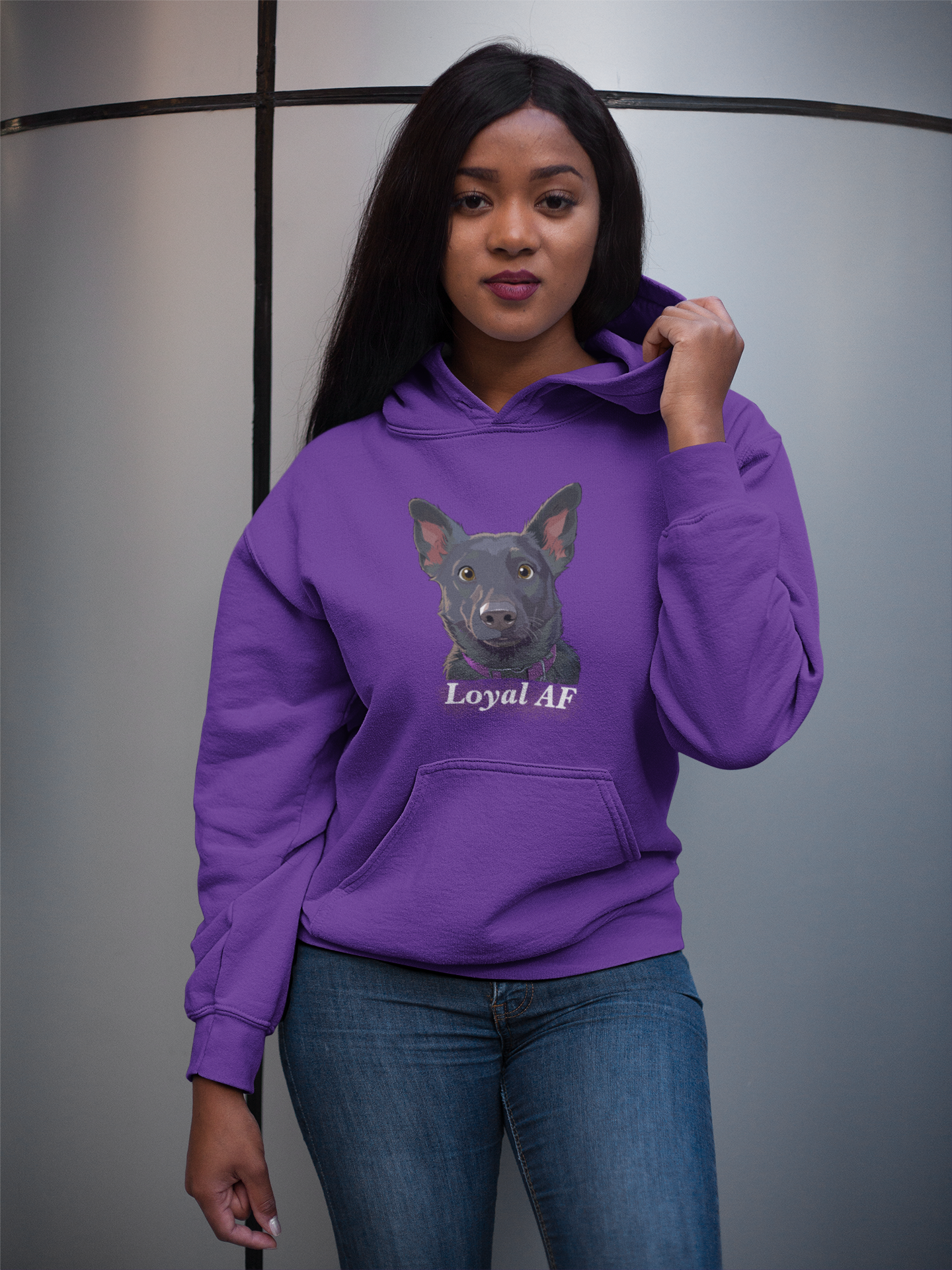 Woman standing near metal column holding up a purple Gildan hoodie featuring the Mathis Loyal AF design
