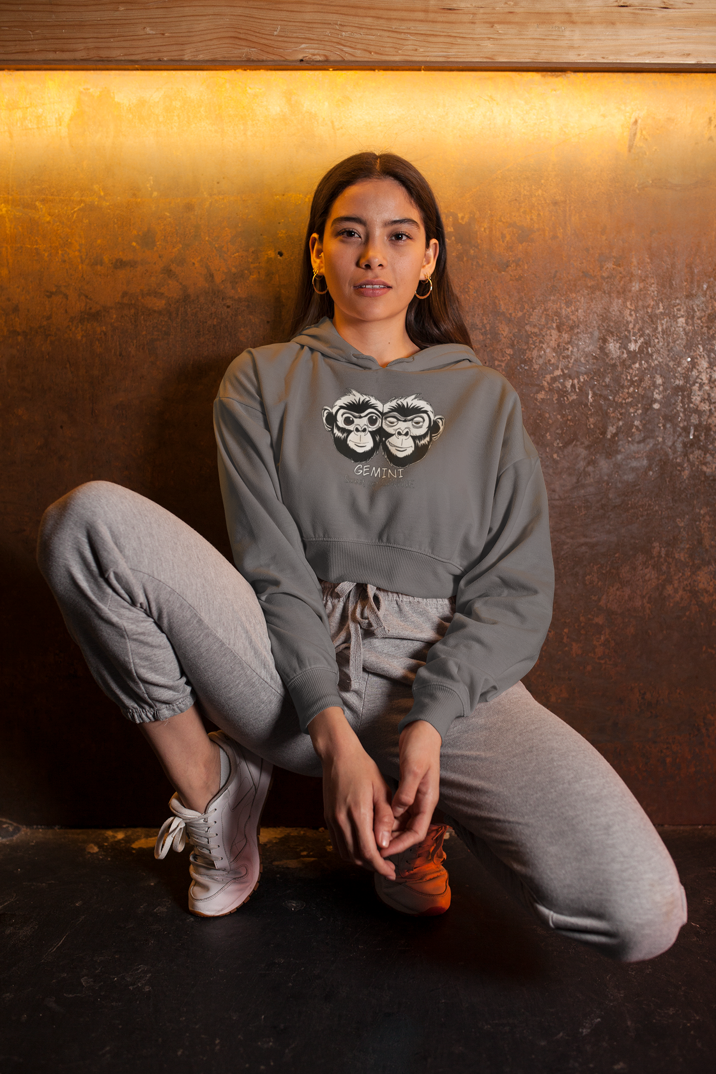 Woman kneeling while wearing a storm blue cropped hoodie featuring the Gemini black and white monkey design