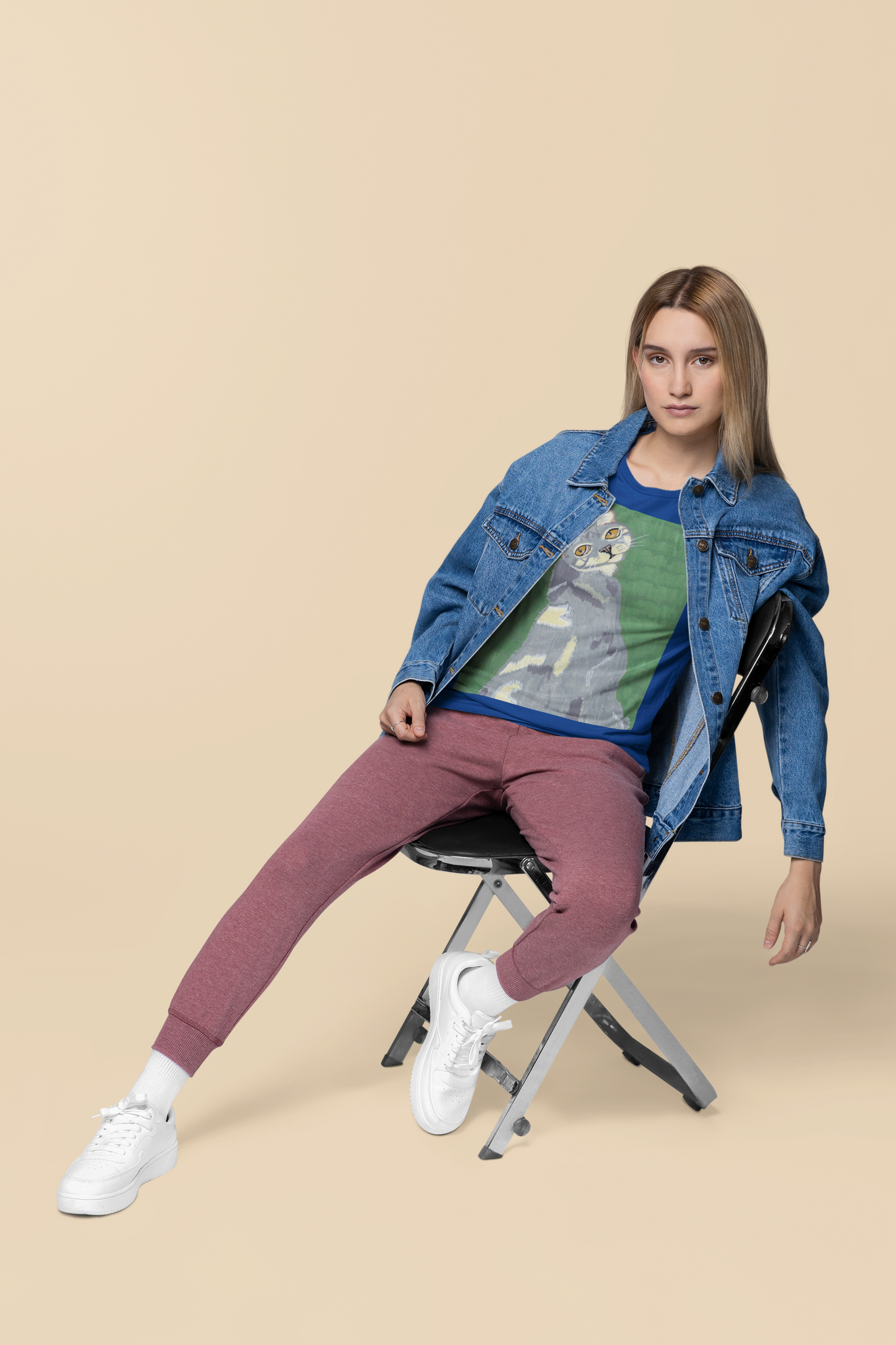 Woman in denim jacket sitting on a chair wearing a true royal blue Bella + Canvas t-shirt featuring Mr. Grey cat portrait from GrungePup