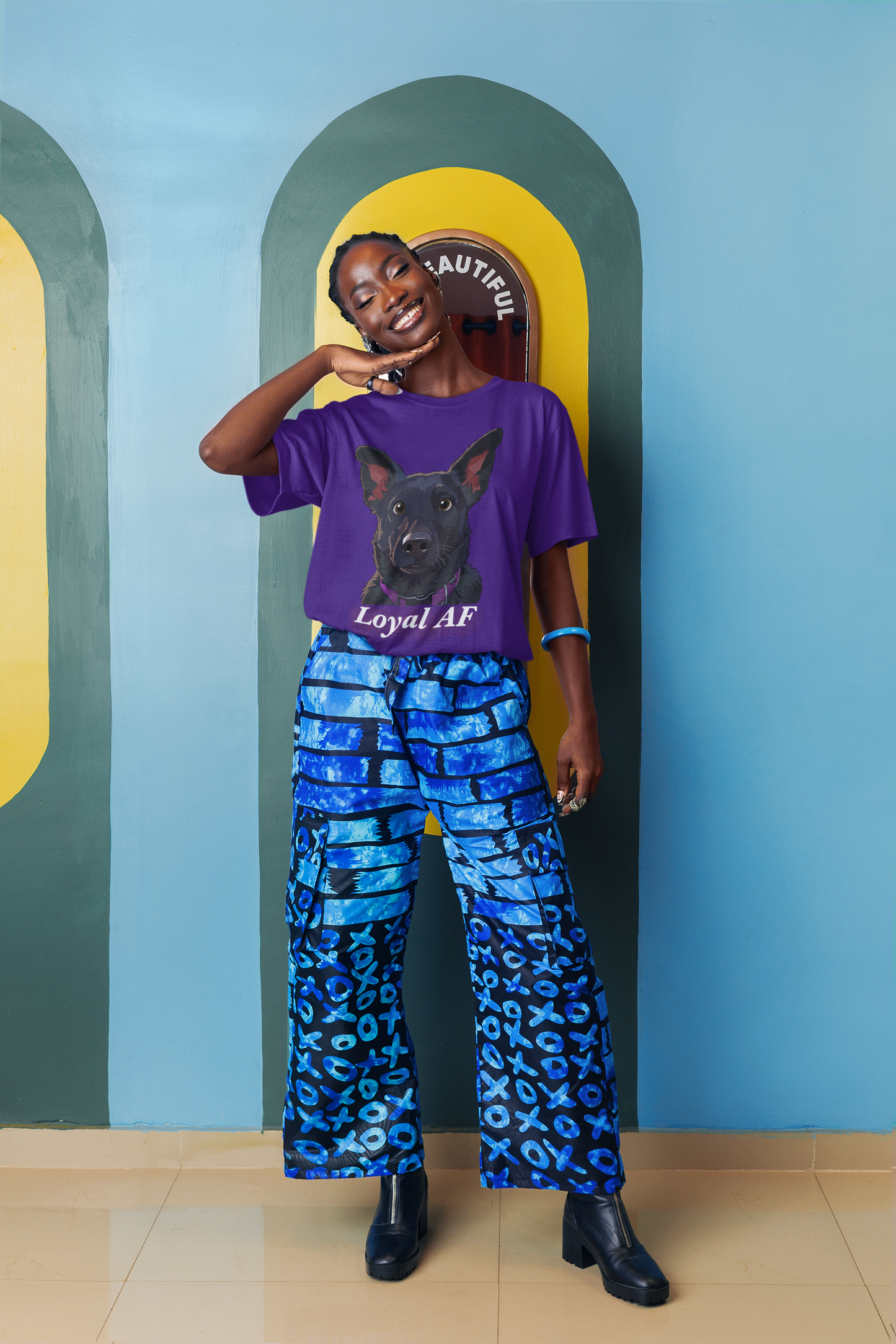 Smiling woman posing against colorful artsy wall wearing a purple Bella + Canvas t-shirt with Mathis Loyal AF portrait